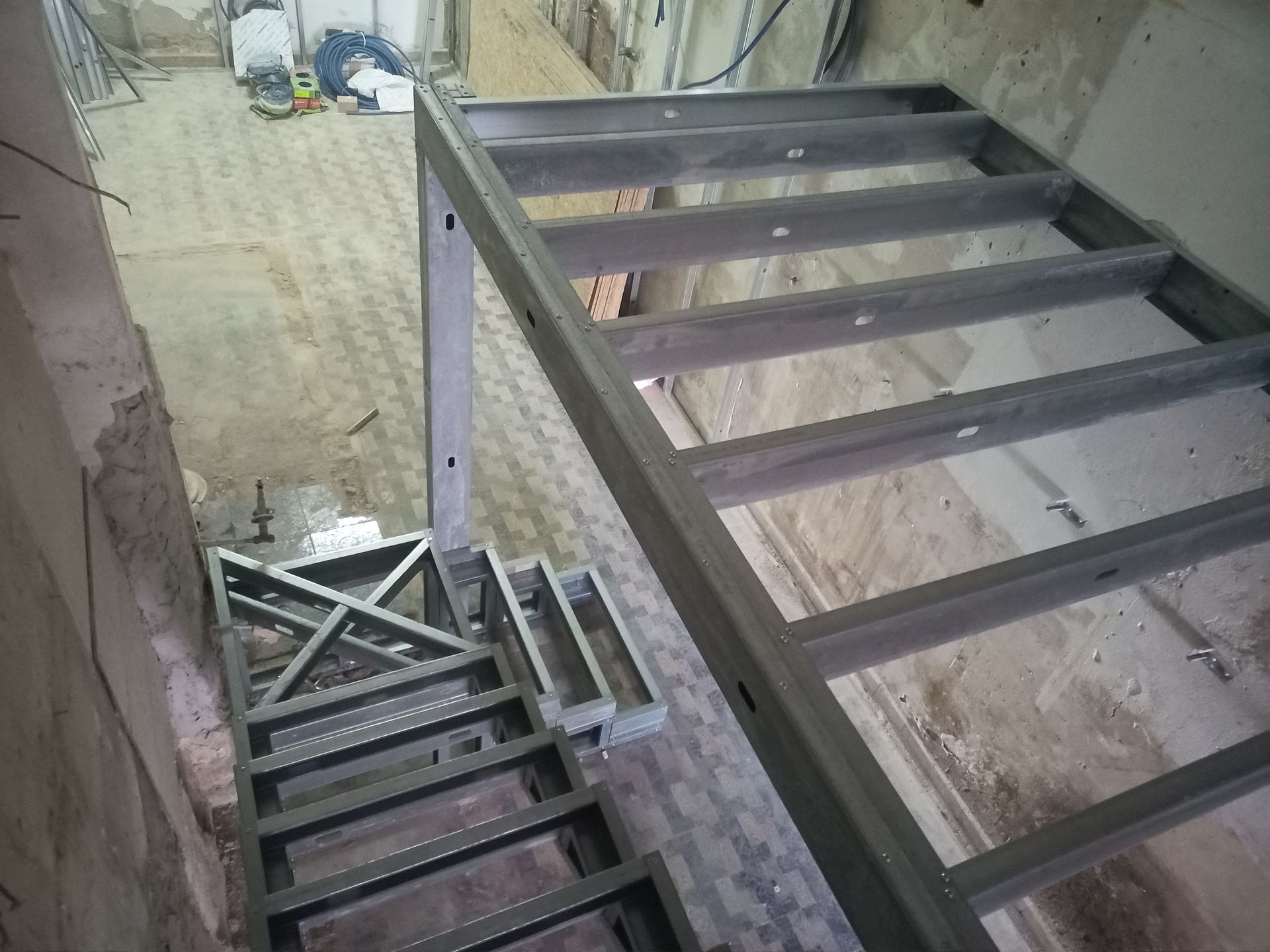 Estrutura metálica de escada em construção dentro de um edifício com paredes e piso em estado bruto.