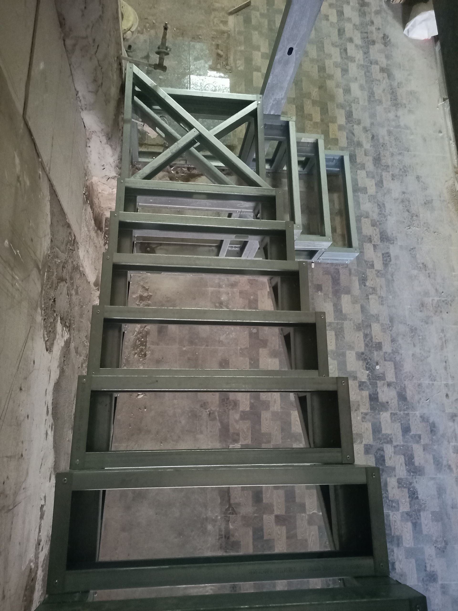 Escada de madeira pintada de cinza, que leva ao andar superior. O vão da escada é escuro e o piso tem um padrão.