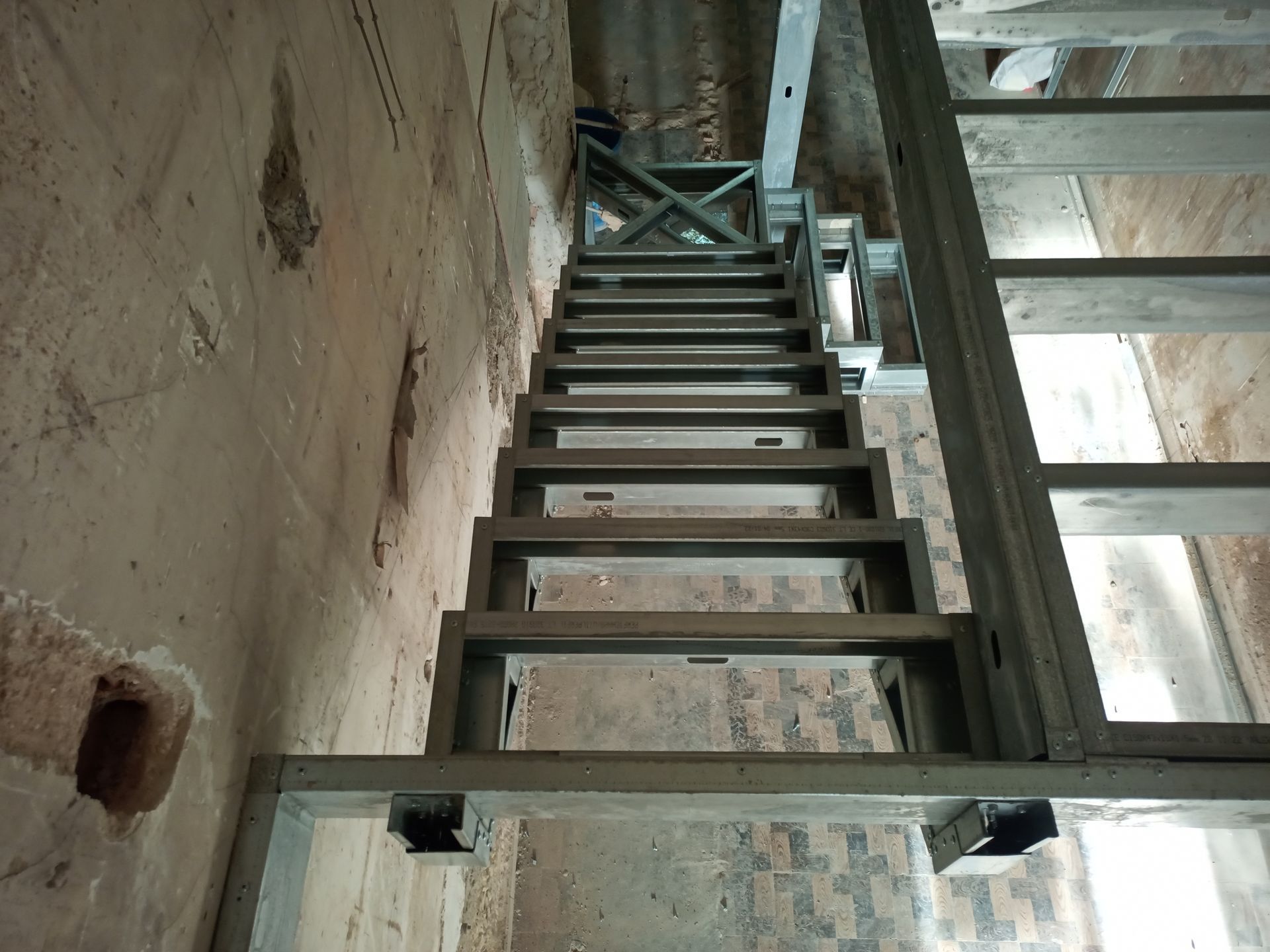 Estrutura metálica de escada em construção em um edifício. Degraus vazios, estrutura de suporte visível, paredes inacabadas.