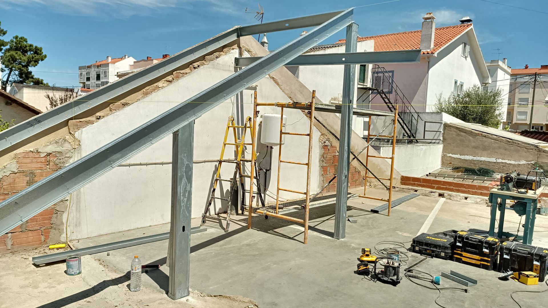 Construção de uma estrutura metálica para painéis solares sobre um telhado de concreto, com andaimes e ferramentas.