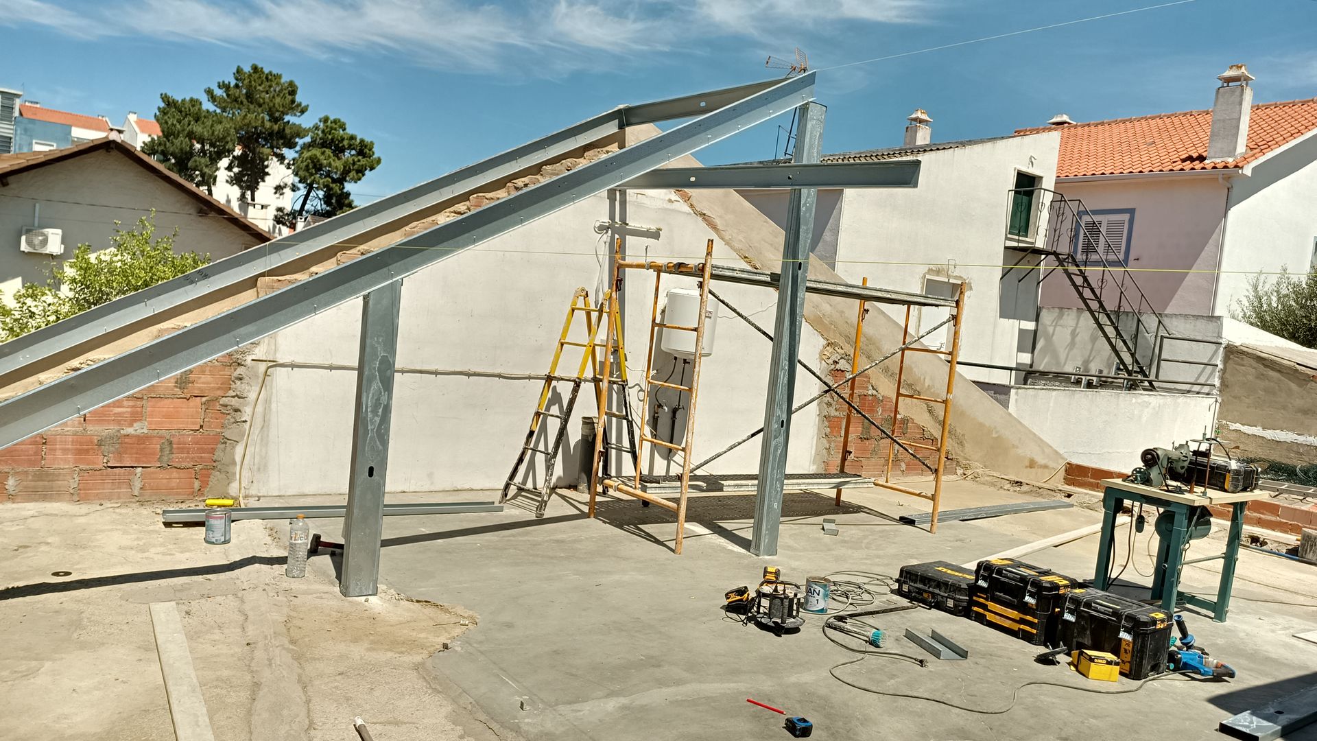 Canteiro de obras: estrutura metálica para painéis solares. Operários em escadas, andaimes encostados em um prédio, ferramentas espalhadas.