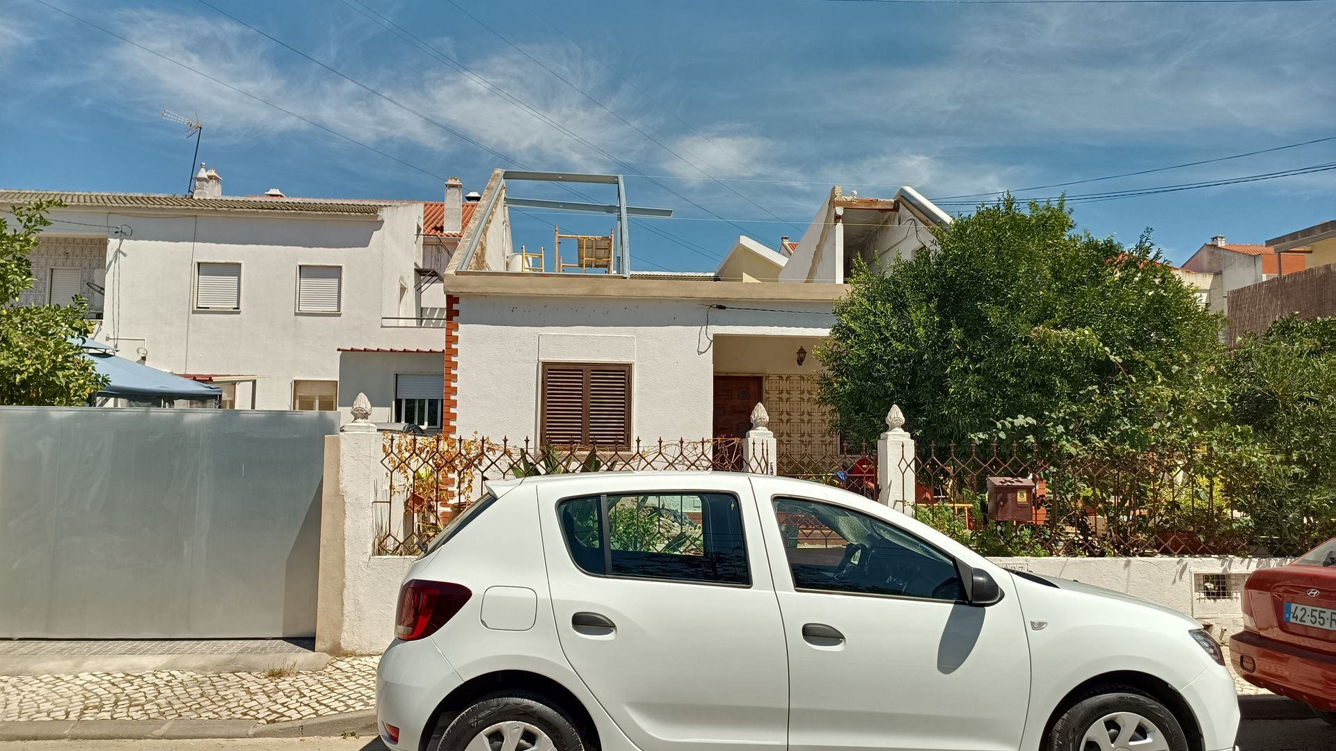 Carro branco estacionado em frente a prédios brancos sob um céu azul.