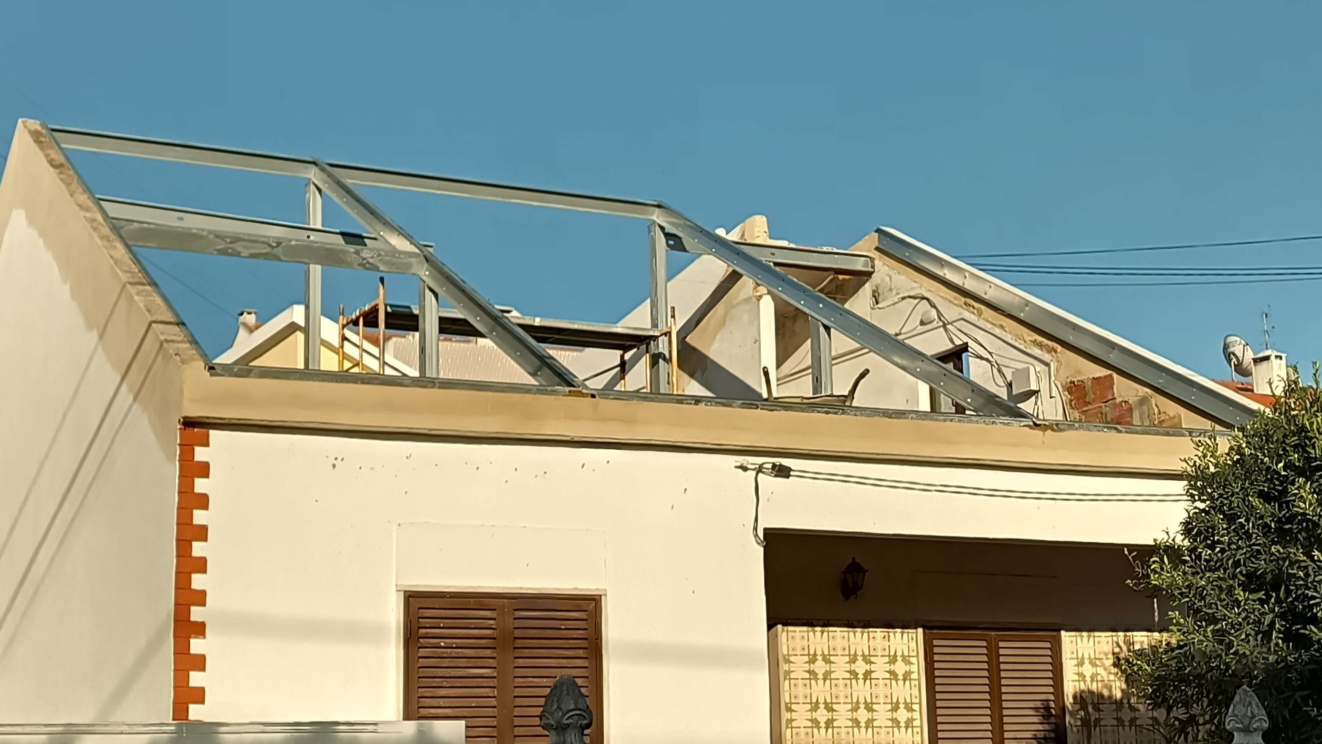 Casa em construção, estrutura do telhado exposta, céu azul.