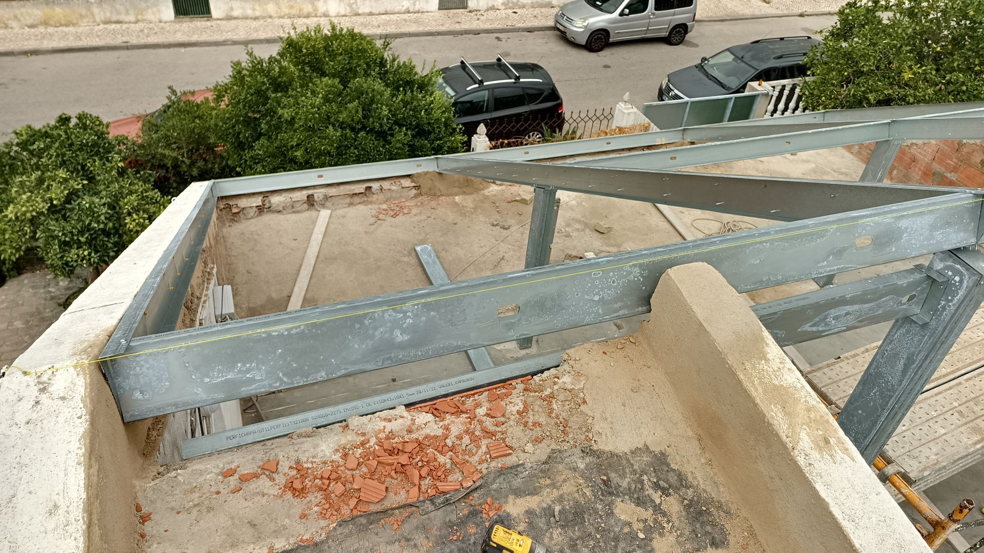 Estrutura metálica sobre um telhado plano, com vista para uma rua com carros estacionados e árvores.