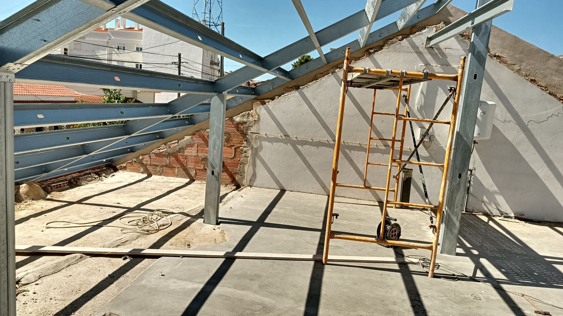 Estrutura metálica e andaimes dentro de um edifício em construção; a luz solar intensa projeta longas sombras.