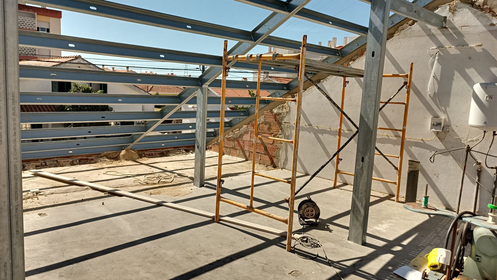 Construção de um edifício com estrutura de aço. Andaimes, piso de concreto, ambiente externo ensolarado.