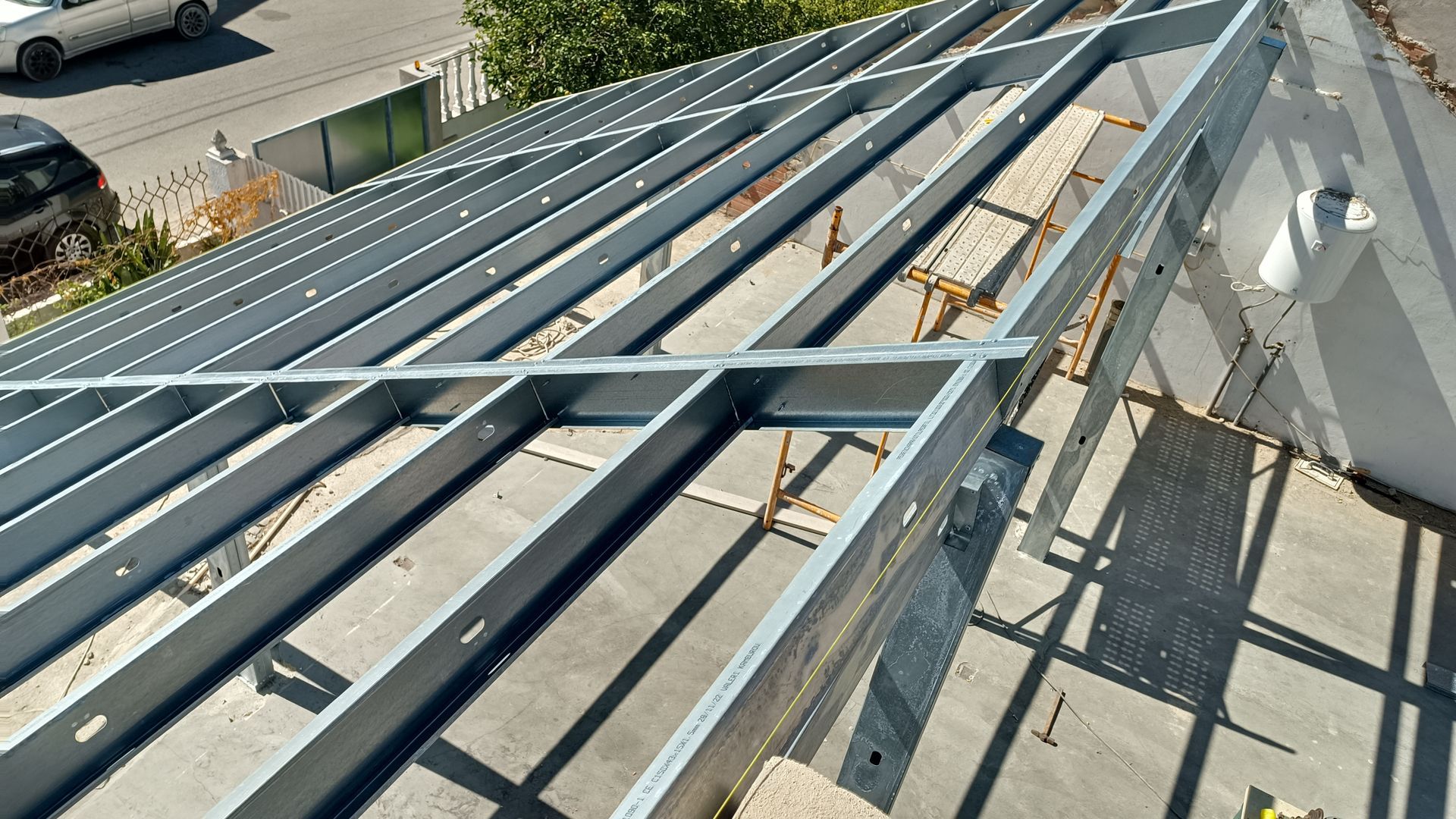 Estrutura metálica de um telhado em construção, com vigas e suportes em ambiente externo.