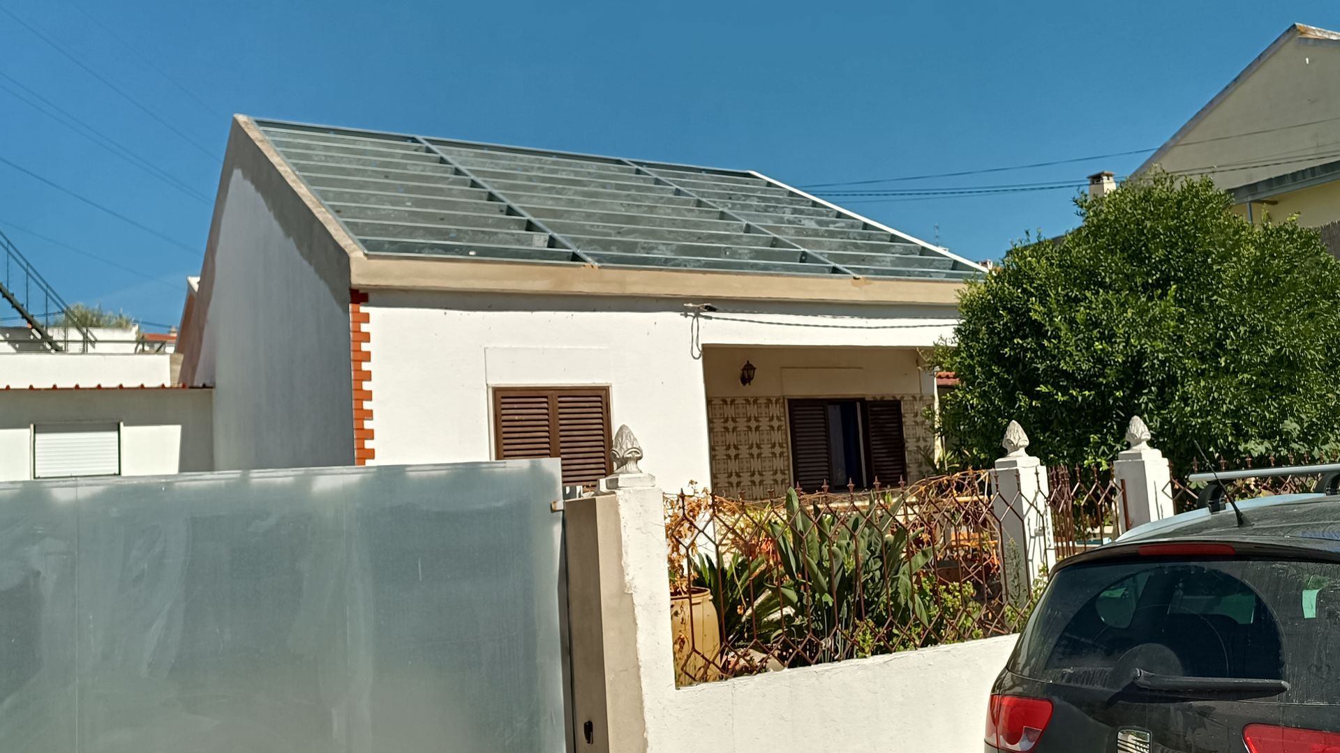 Casa branca com telhado cinza, pequeno jardim e carro estacionado em frente.