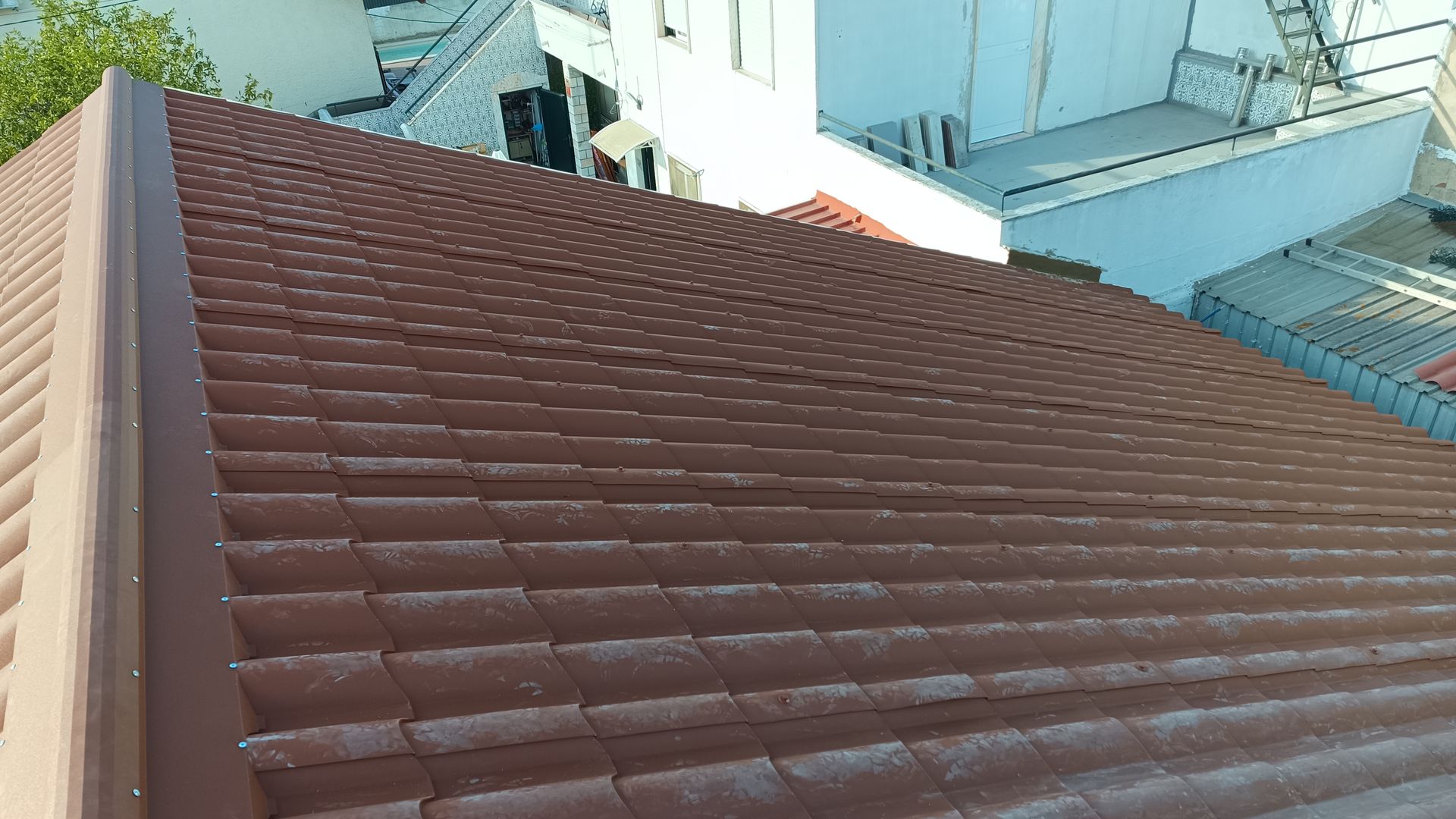 Telhado de telhas marrons de um prédio com paisagem urbana ao fundo em um dia ensolarado.