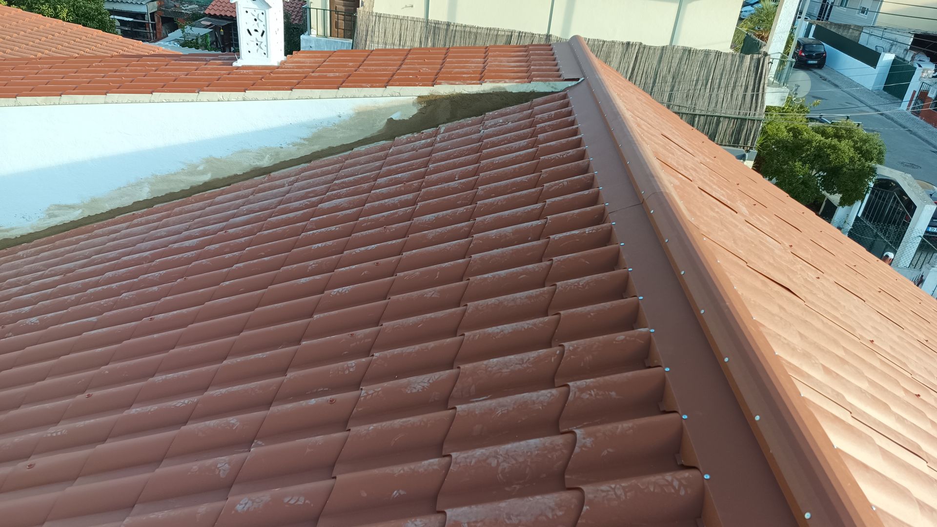 Telhado de telhas marrons com acabamento metálico, visto de cima, em área residencial.