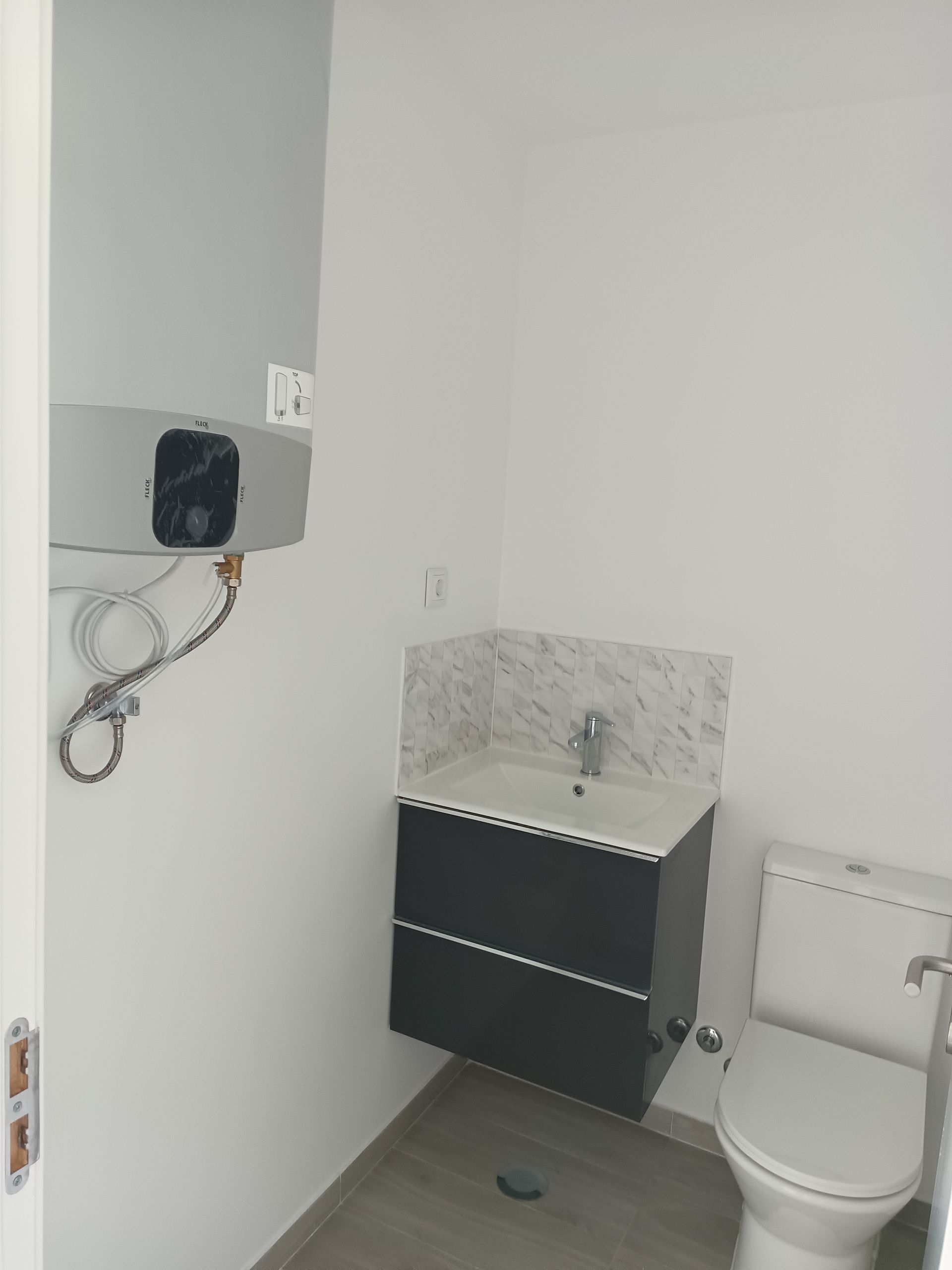 Banheiro pequeno com vaso sanitário, armário escuro e aquecedor de água em uma parede branca.