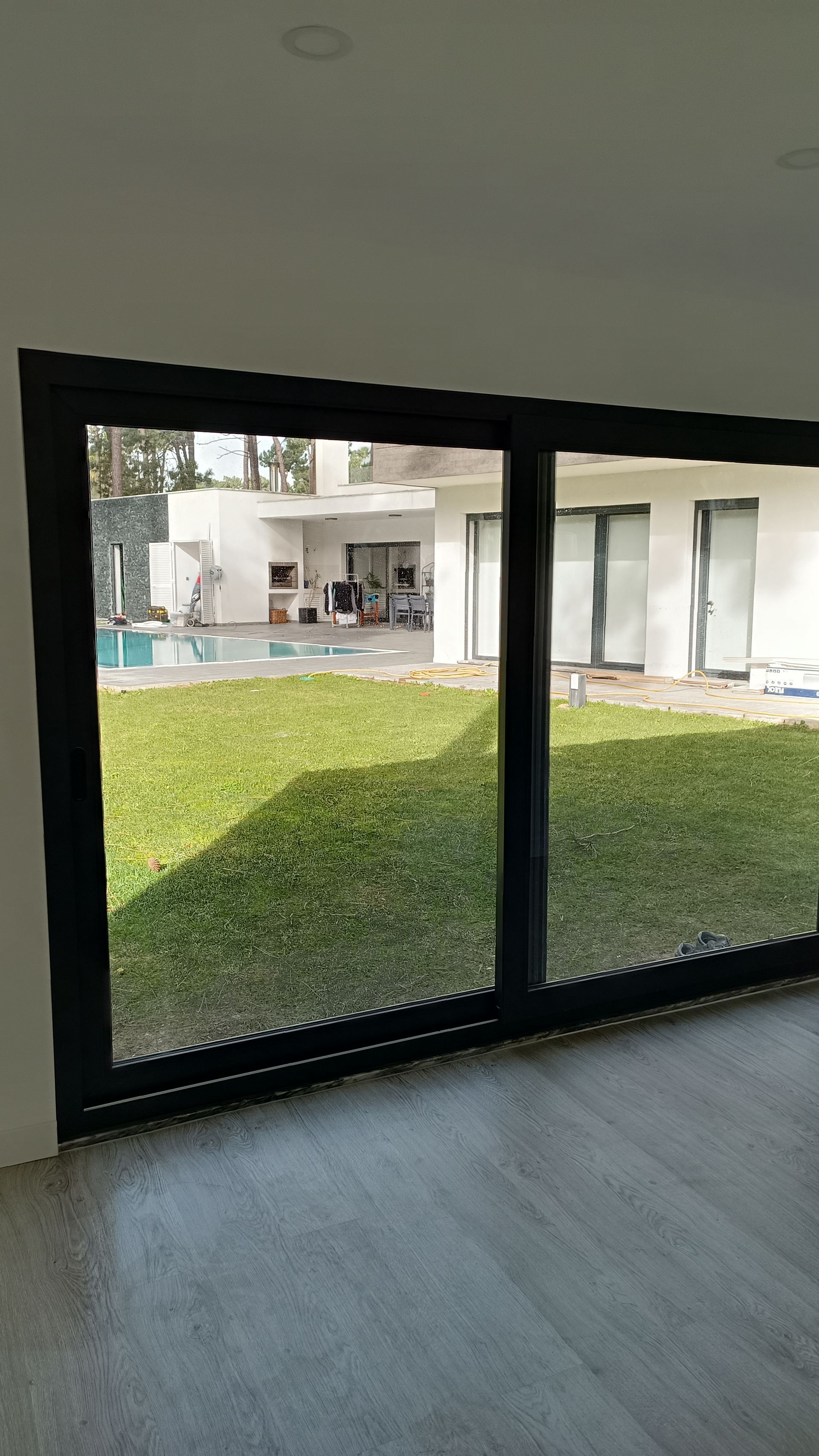 Porta de correr de vidro com moldura preta, com vista para o quintal, piscina e casa. Grama verde no quintal, piso claro no interior.