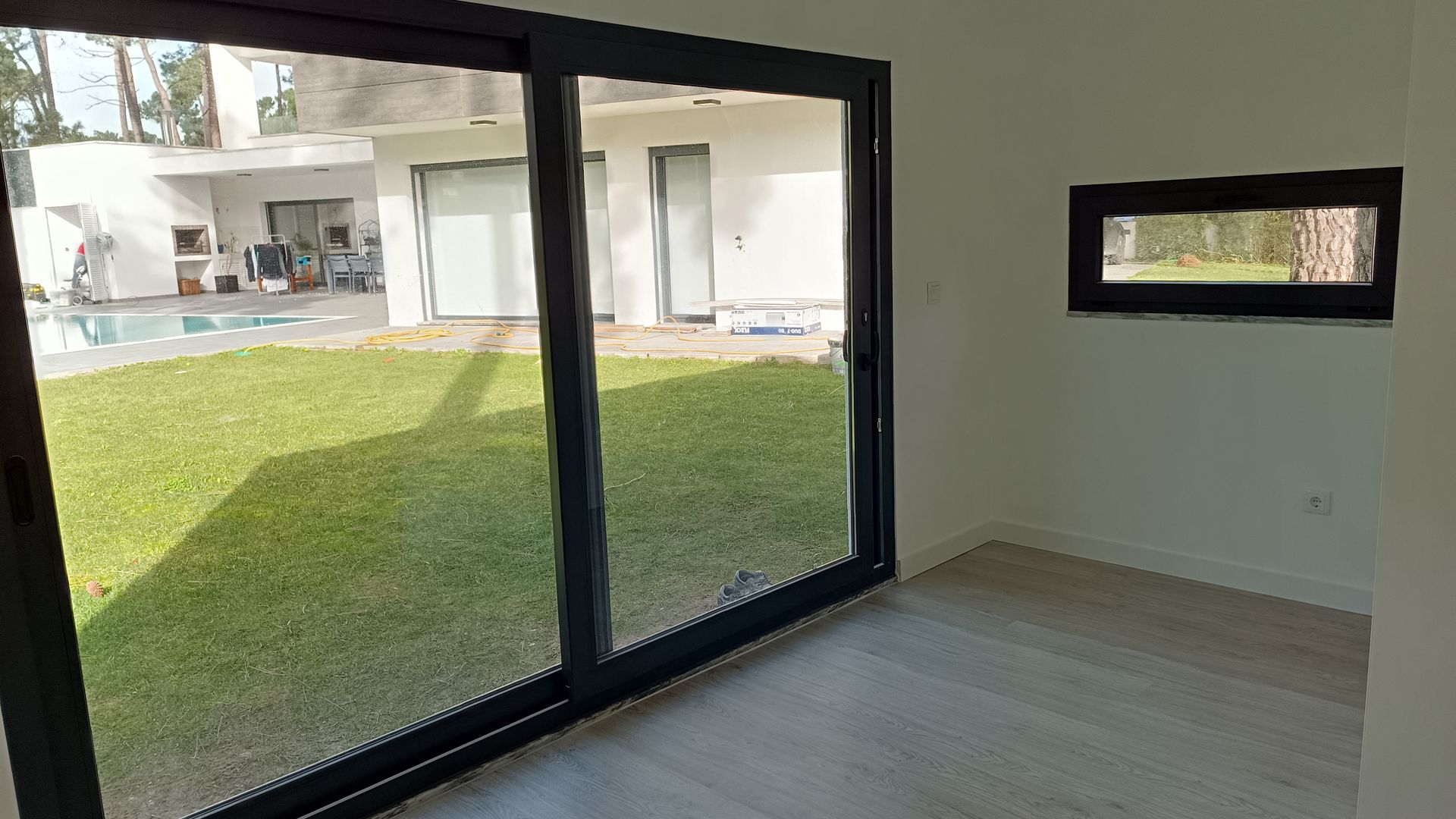 Vista interior de um quarto com grandes portas de vidro deslizantes que dão para um quintal com piscina.