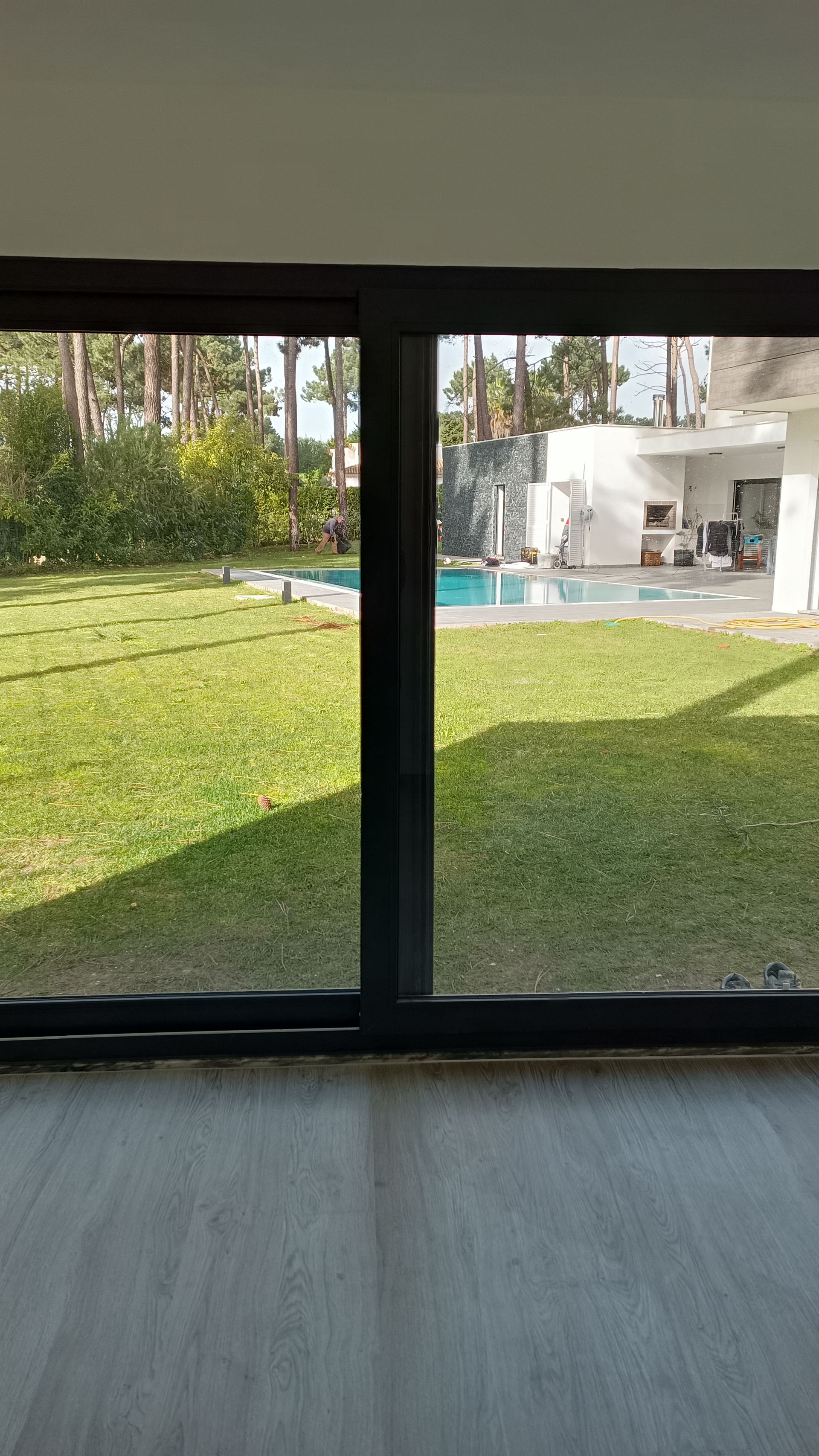 Vista de um quintal com grama verde, piscina e casa através de uma grande janela.