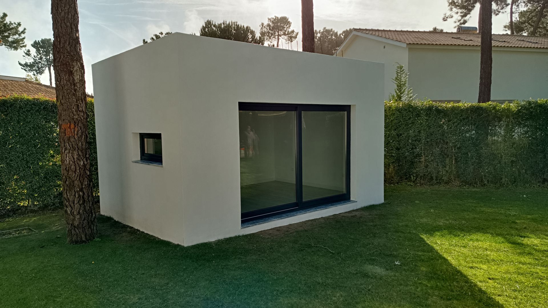 Prédio branco, cúbico, com grandes portas de vidro deslizantes e uma pequena janela, em um gramado com árvores.