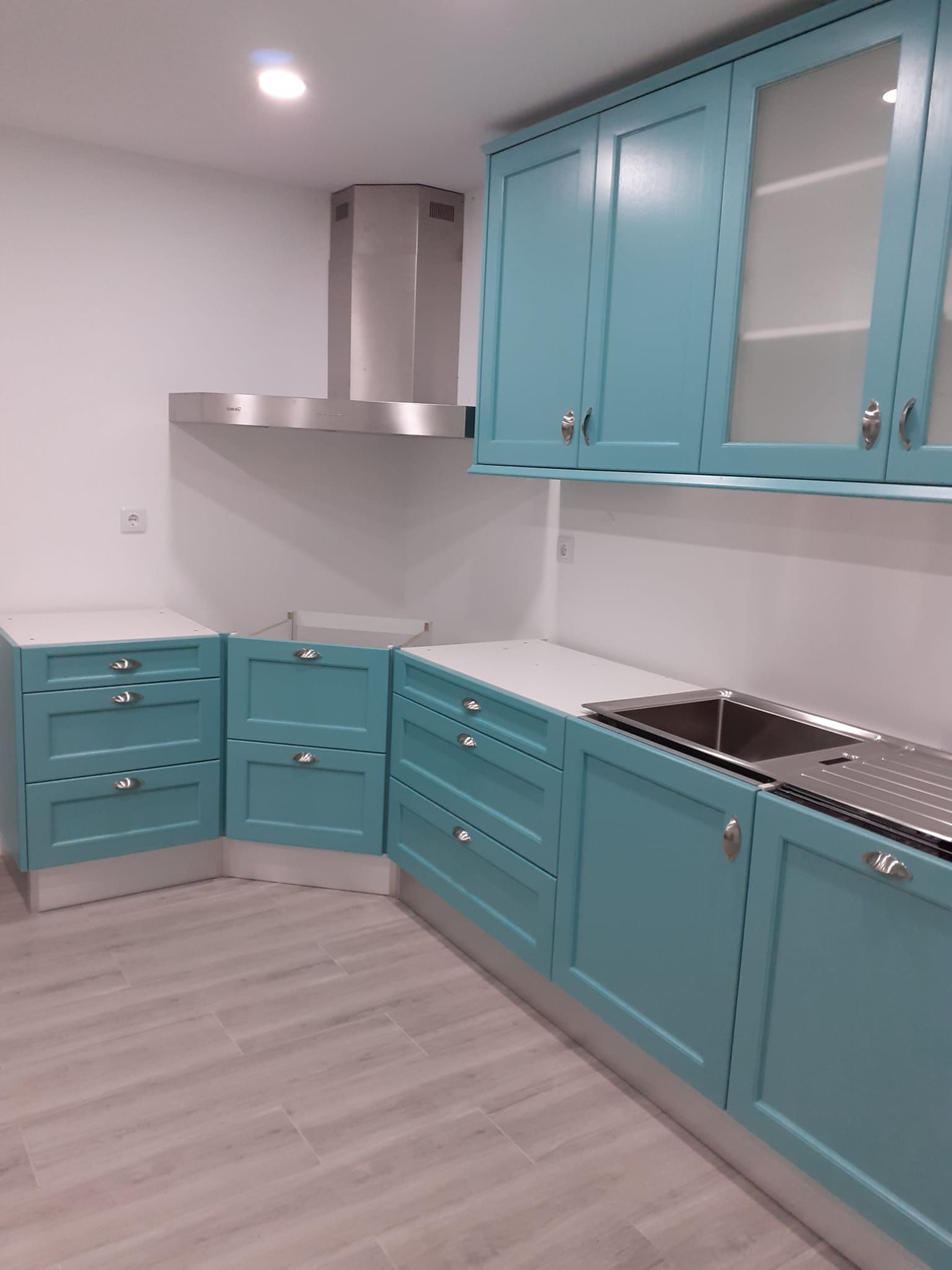 Armários de cozinha azuis com bancadas brancas e eletrodomésticos de aço inoxidável.