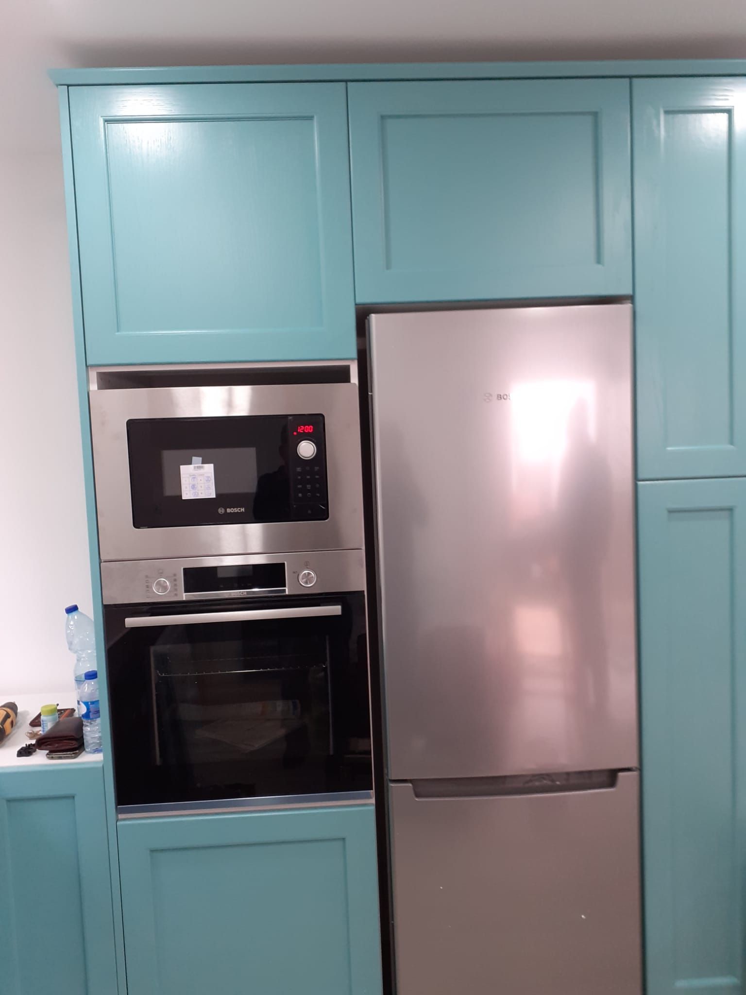 Armários de cozinha azuis com forno e micro-ondas embutidos, ao lado de uma geladeira de aço inoxidável.