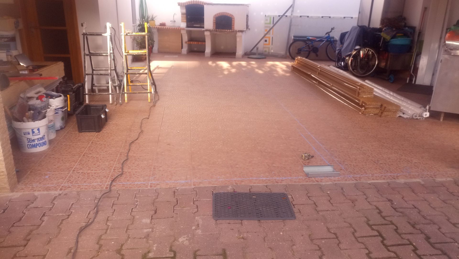 Vista de um pátio com superfície de cascalho rosa, forno externo e materiais de construção.