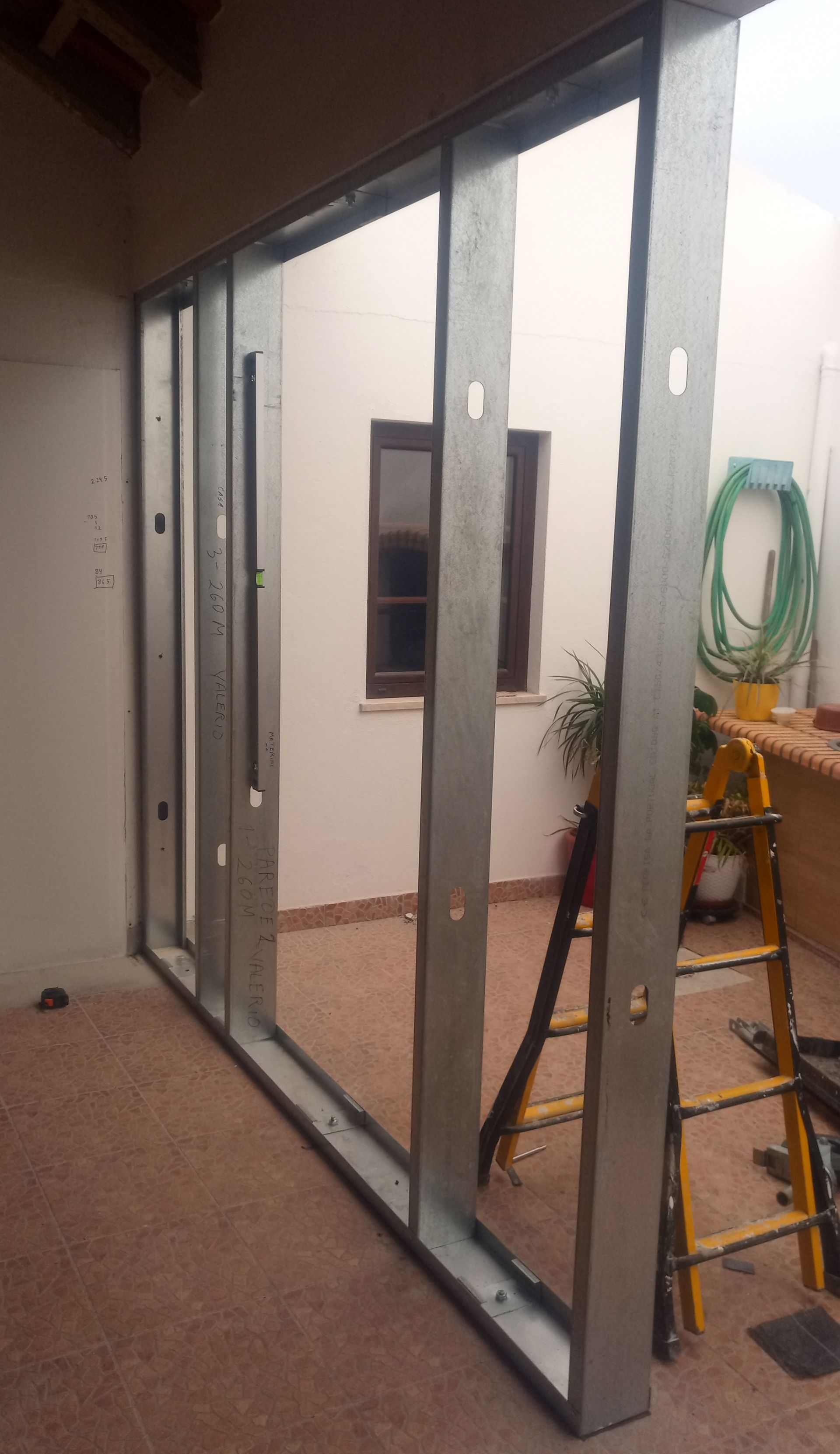 Estrutura metálica para uma parede em um ambiente externo, com uma escada e um prédio ao fundo.