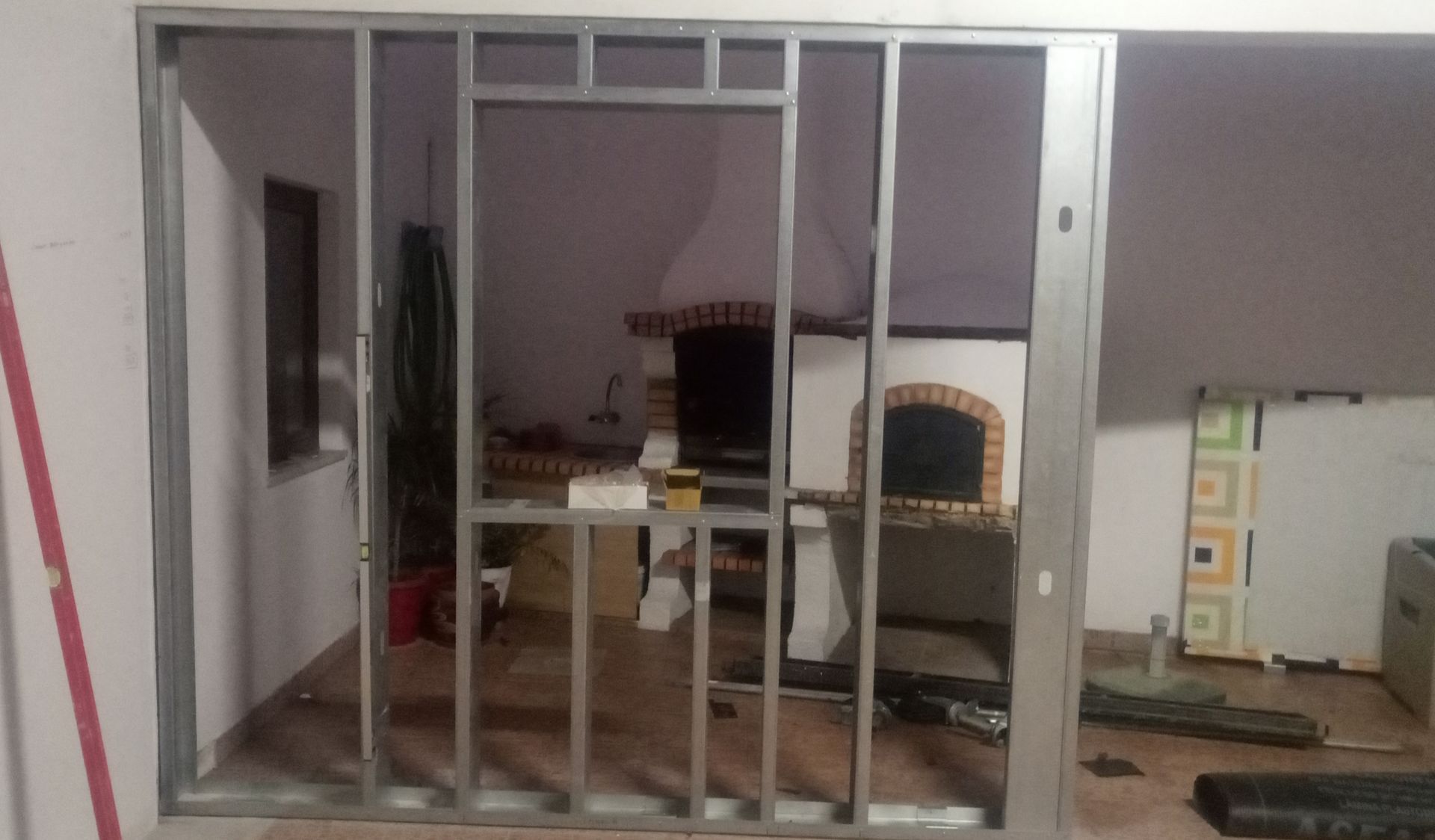 Estrutura metálica de uma parede em construção, com uma lareira visível através da abertura.