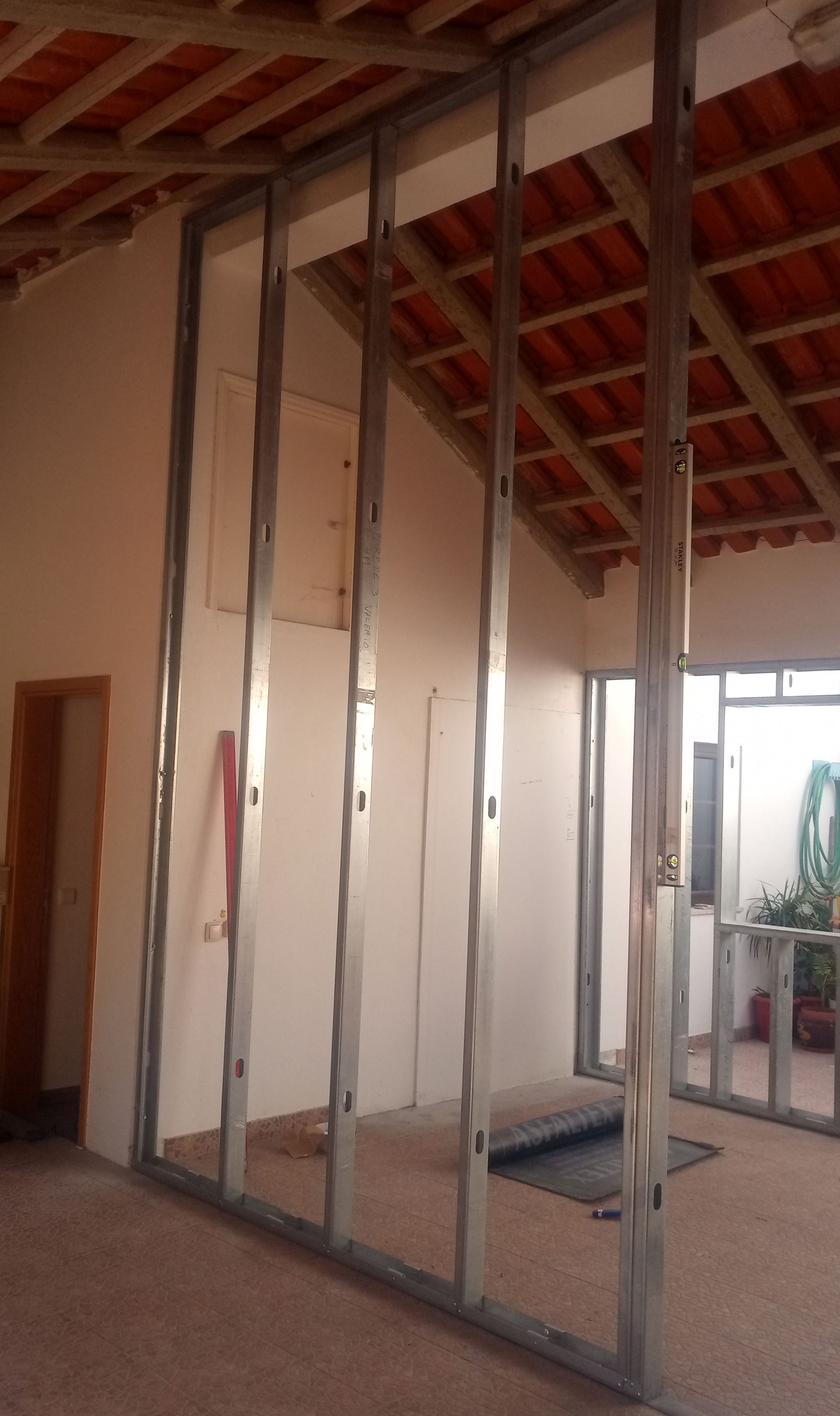 Estrutura metálica para uma parede interna em construção; estrutura do telhado e paredes existentes visíveis.