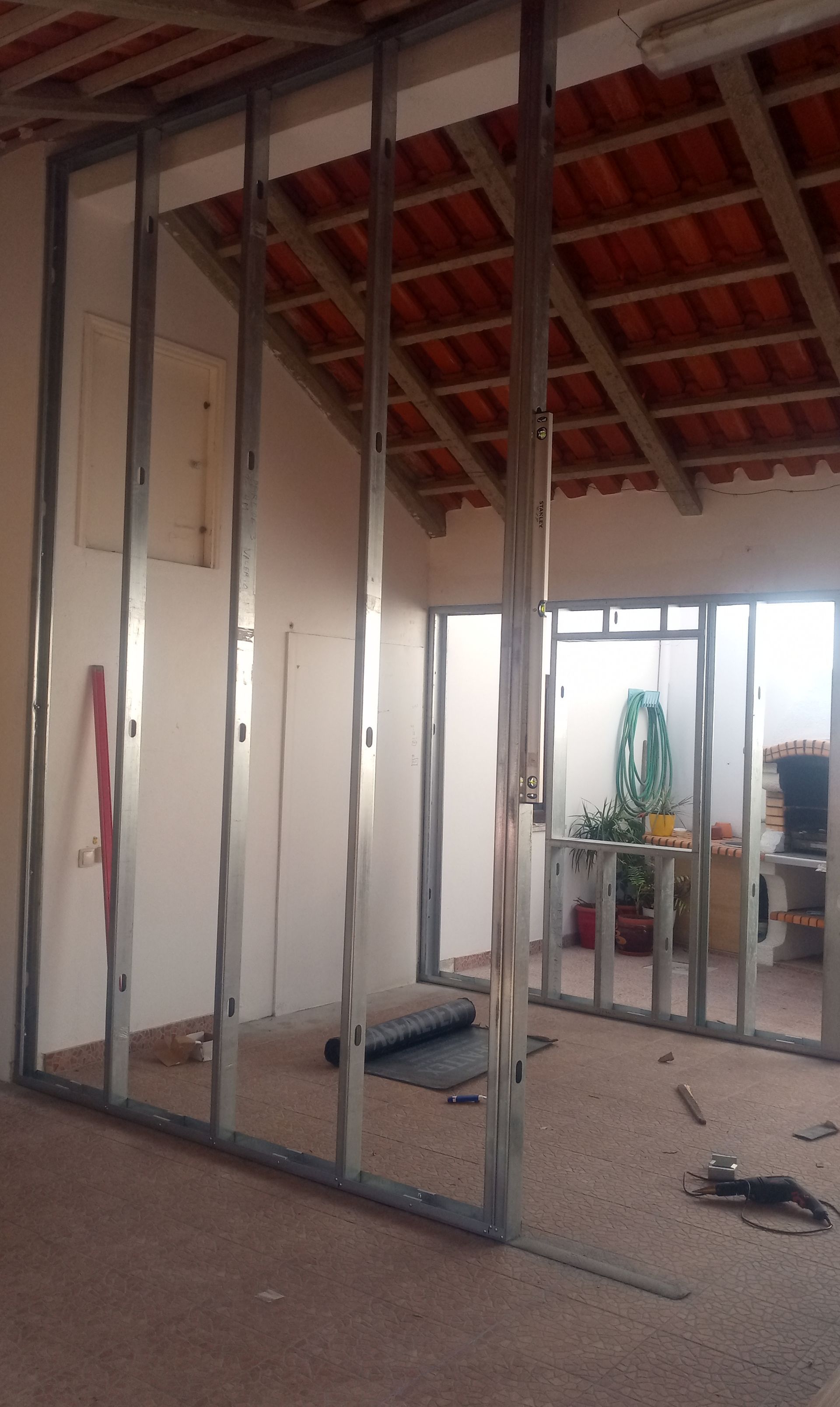 A estrutura das paredes internas é composta por perfis metálicos visíveis contra o telhado de telhas vermelhas e o interior inacabado.