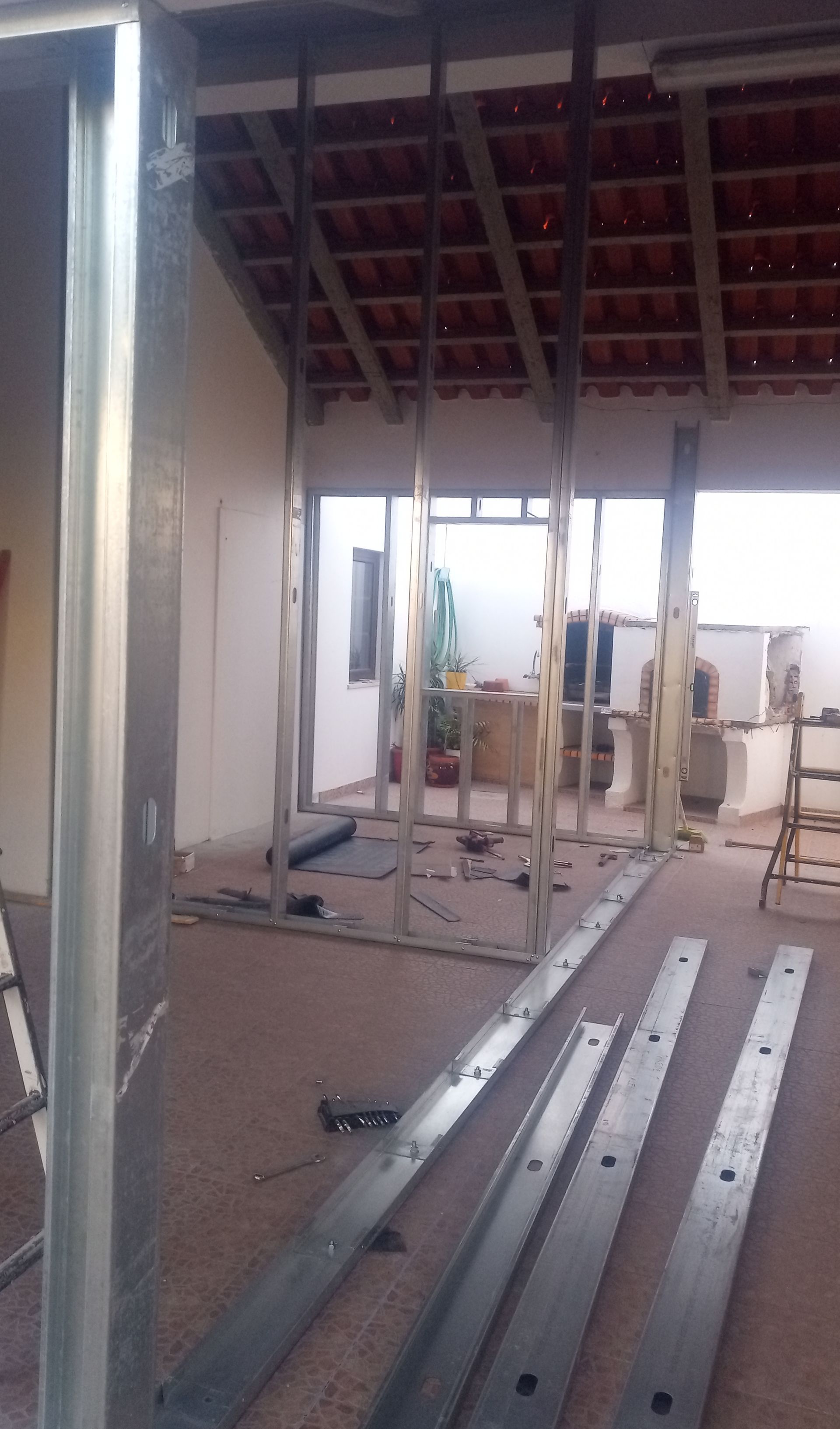 Canteiro de obras interno com estrutura metálica. Espaço aberto com telhas aparentes.