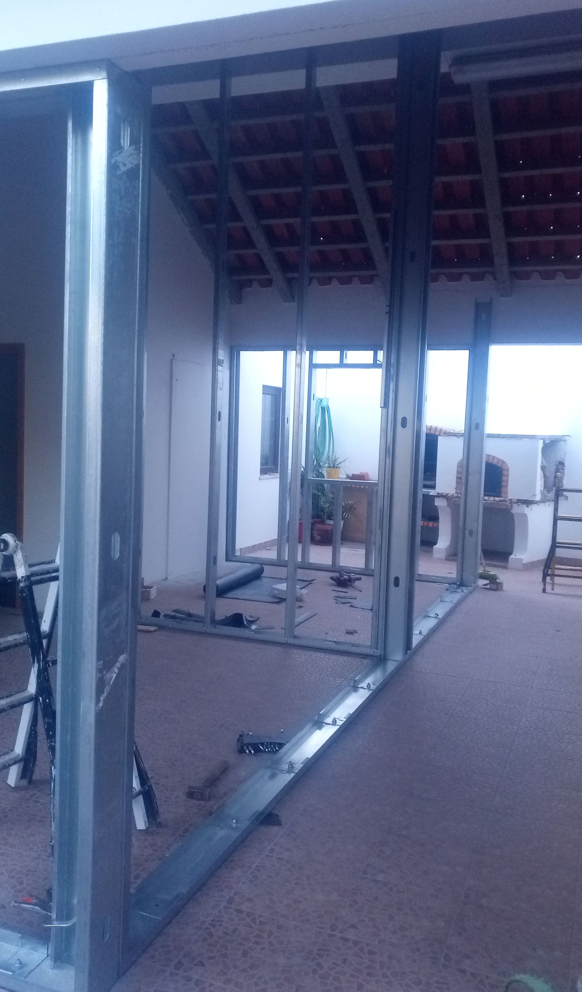 Estrutura metálica para uma parede em construção, revelando um espaço aberto com telhado e quintal visíveis.