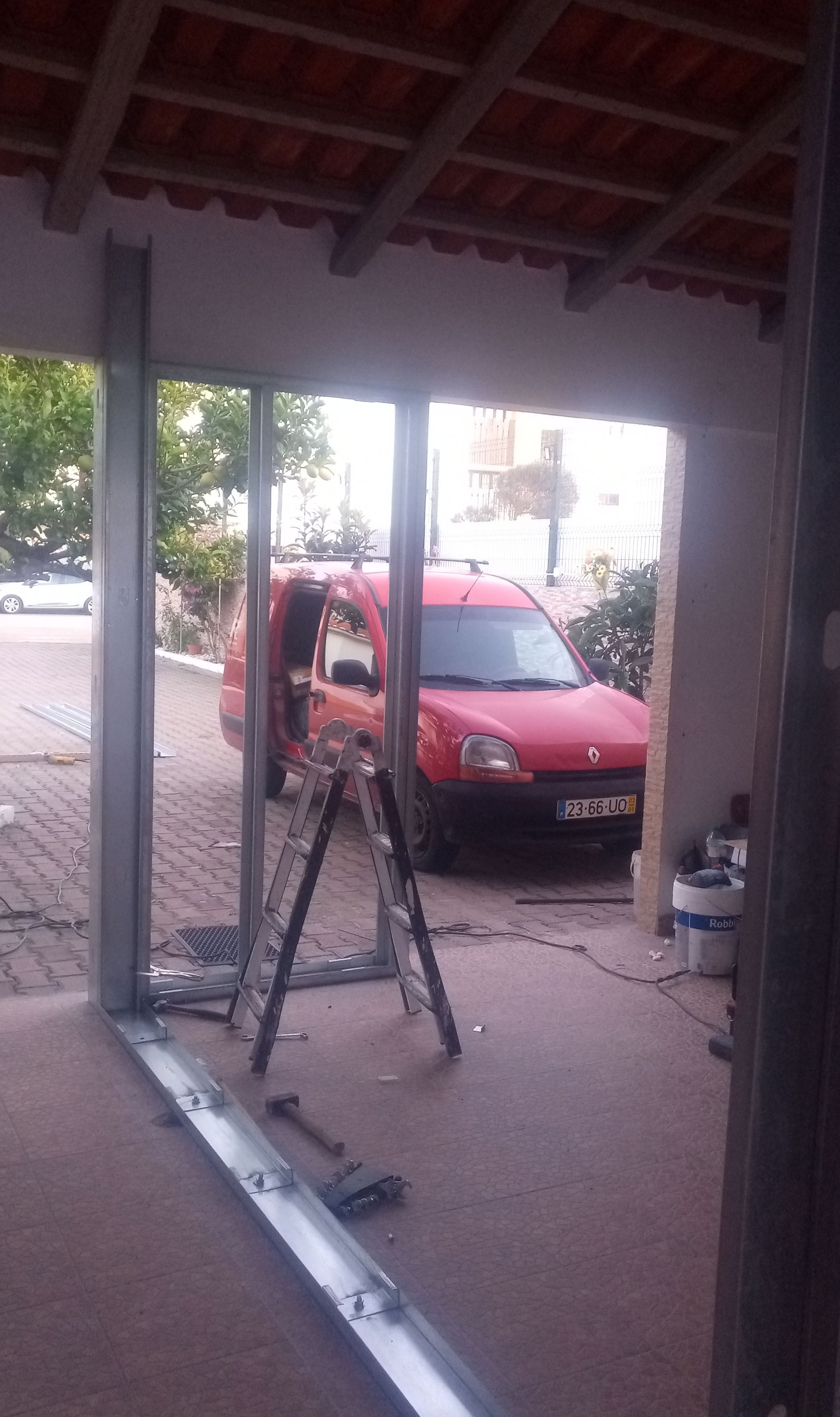 Estrutura metálica com uma van vermelha ao fundo. Uma escada e ferramentas são visíveis.