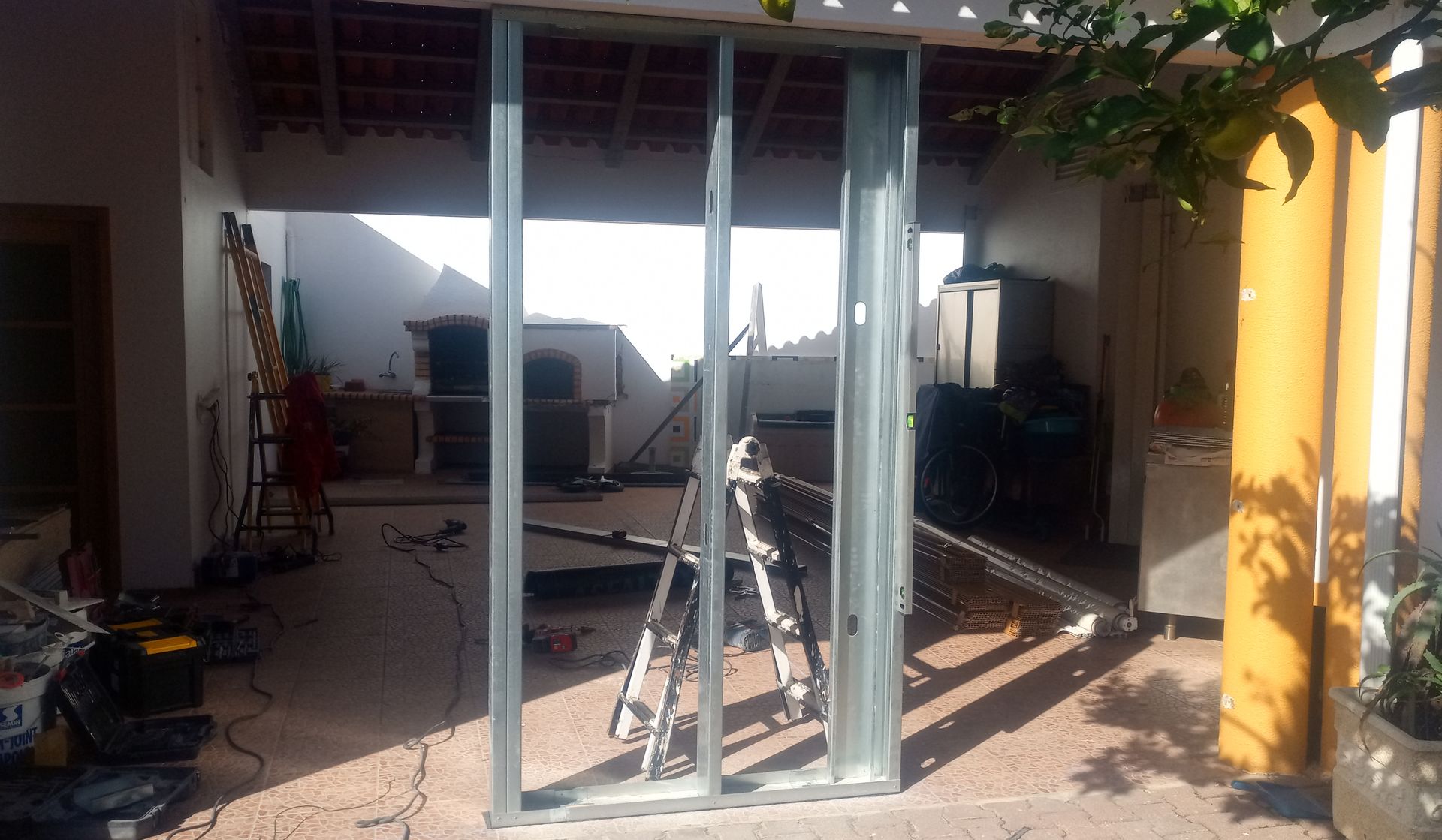 Estrutura metálica para uma parede em construção ao ar livre, contra uma parede branca. A luz do sol penetra através dela.