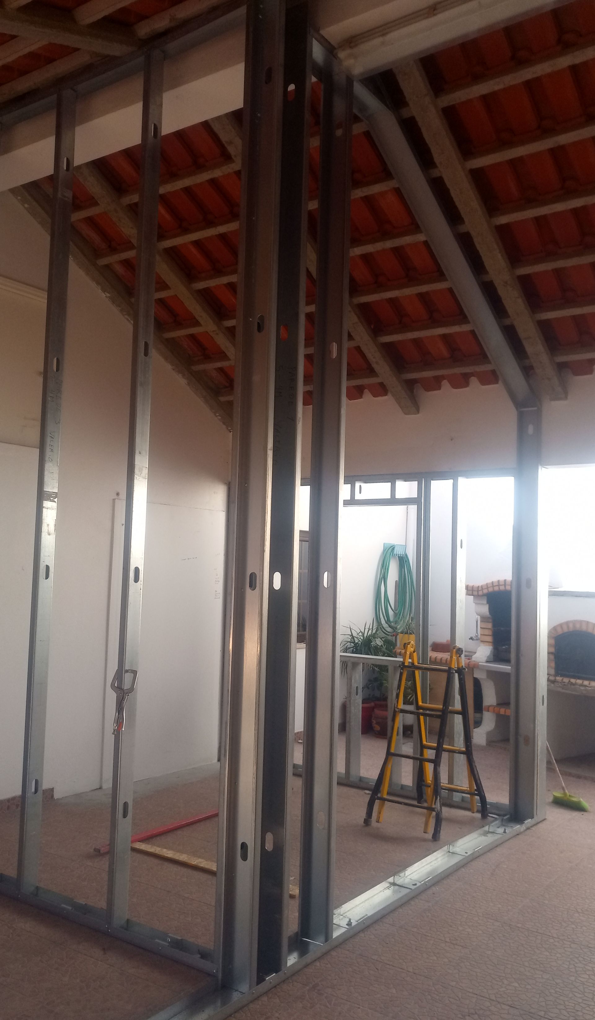 Estrutura metálica para uma parede interna em construção, vigas visíveis e vislumbre do exterior através de aberturas.