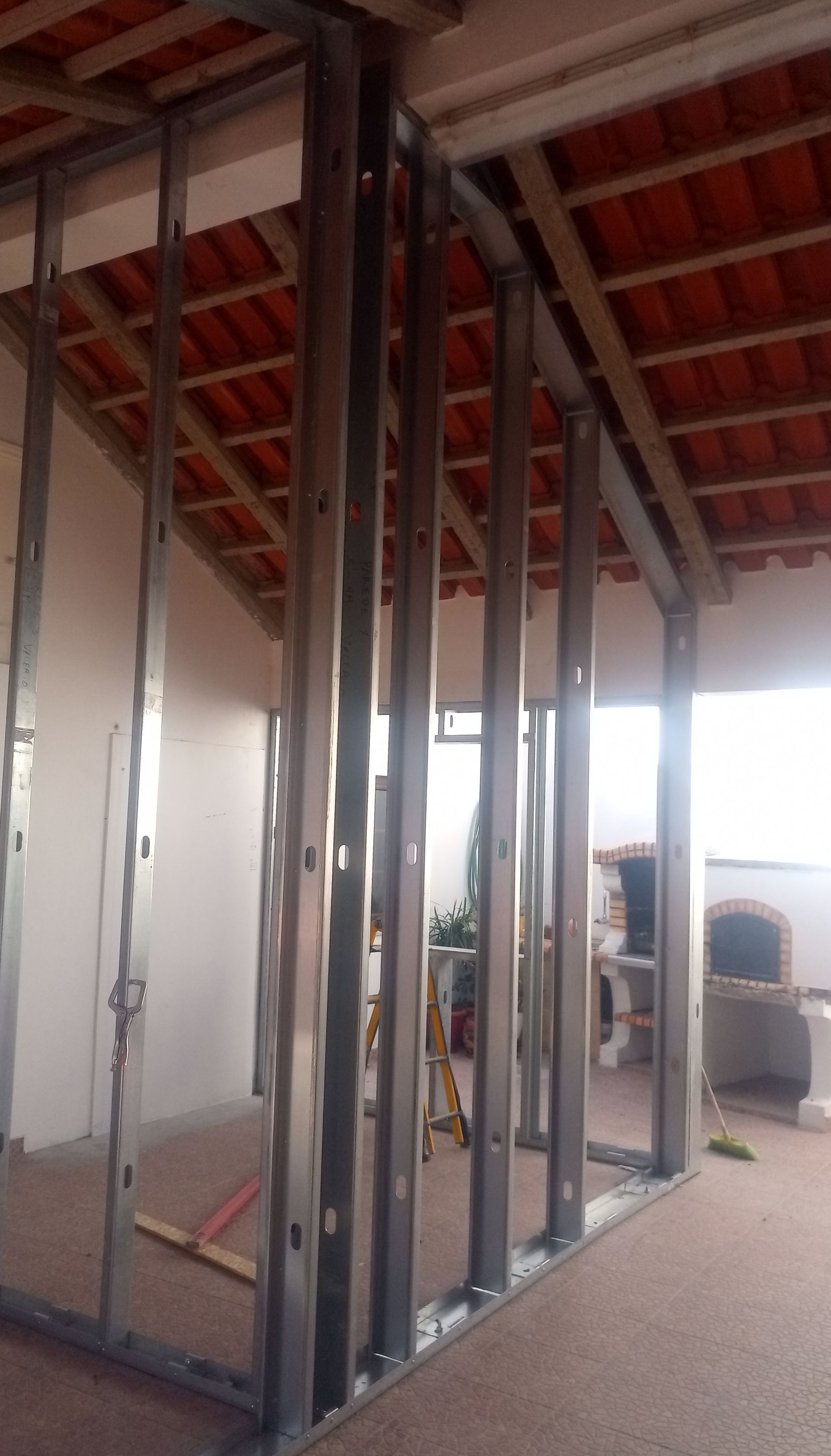 Estrutura metálica de uma parede e teto; vista interior com telhado de telha vermelha visível.