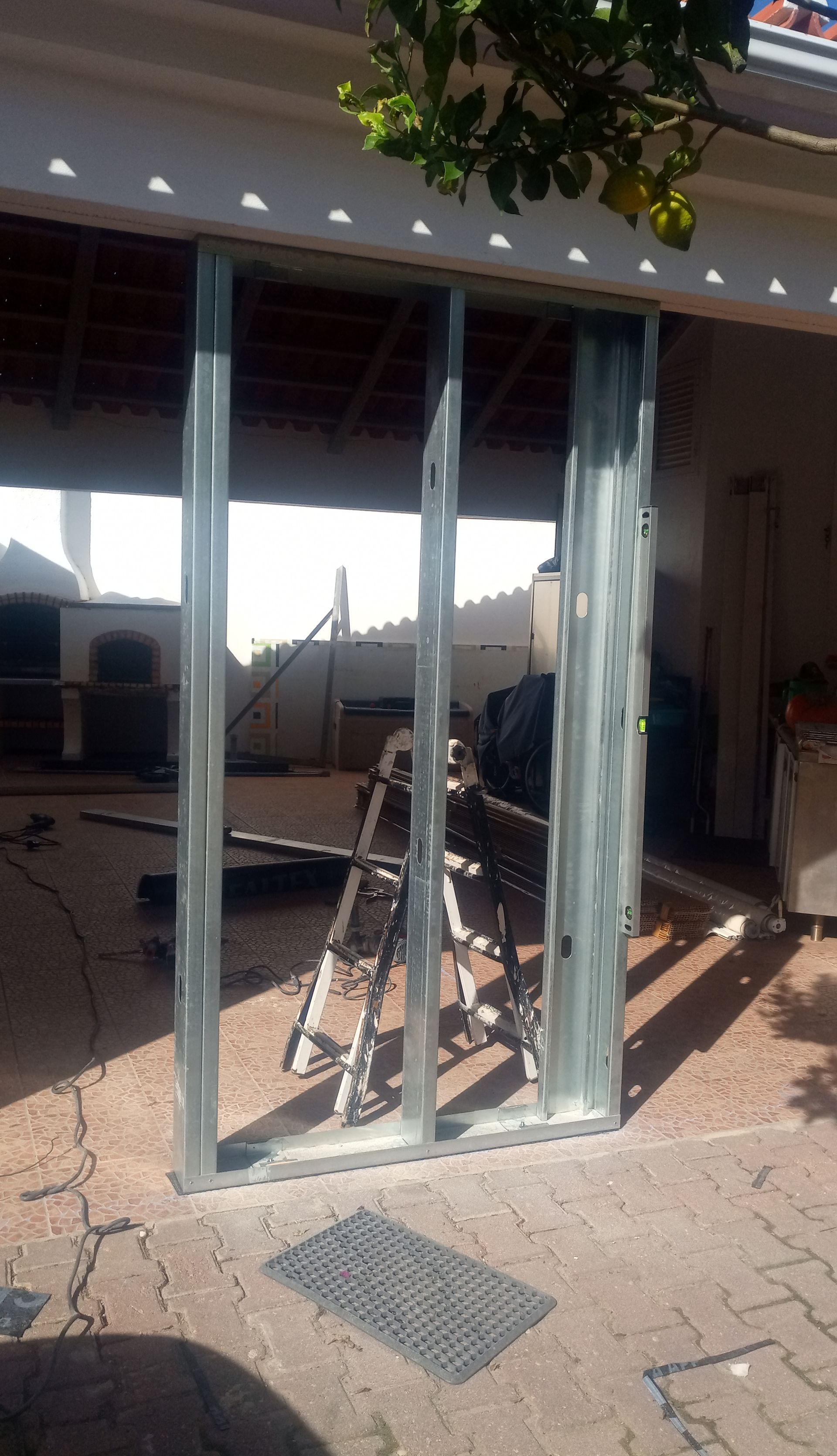 Estrutura metálica de uma porta de correr, instalada ao ar livre em um pátio pavimentado, com uma escada ao fundo.