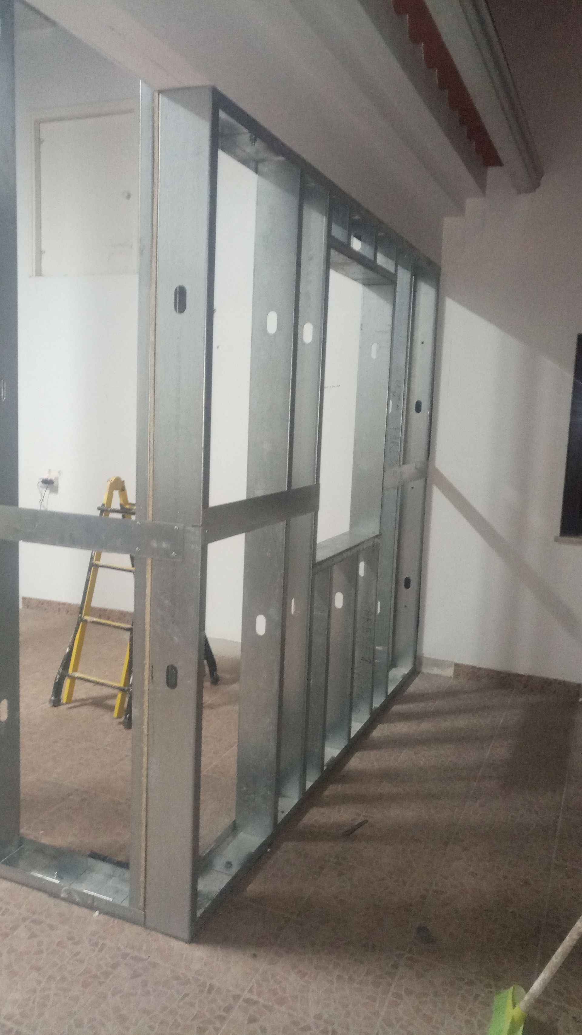 Estrutura metálica de uma parede interna com abertura para janela, em construção em um cômodo.
