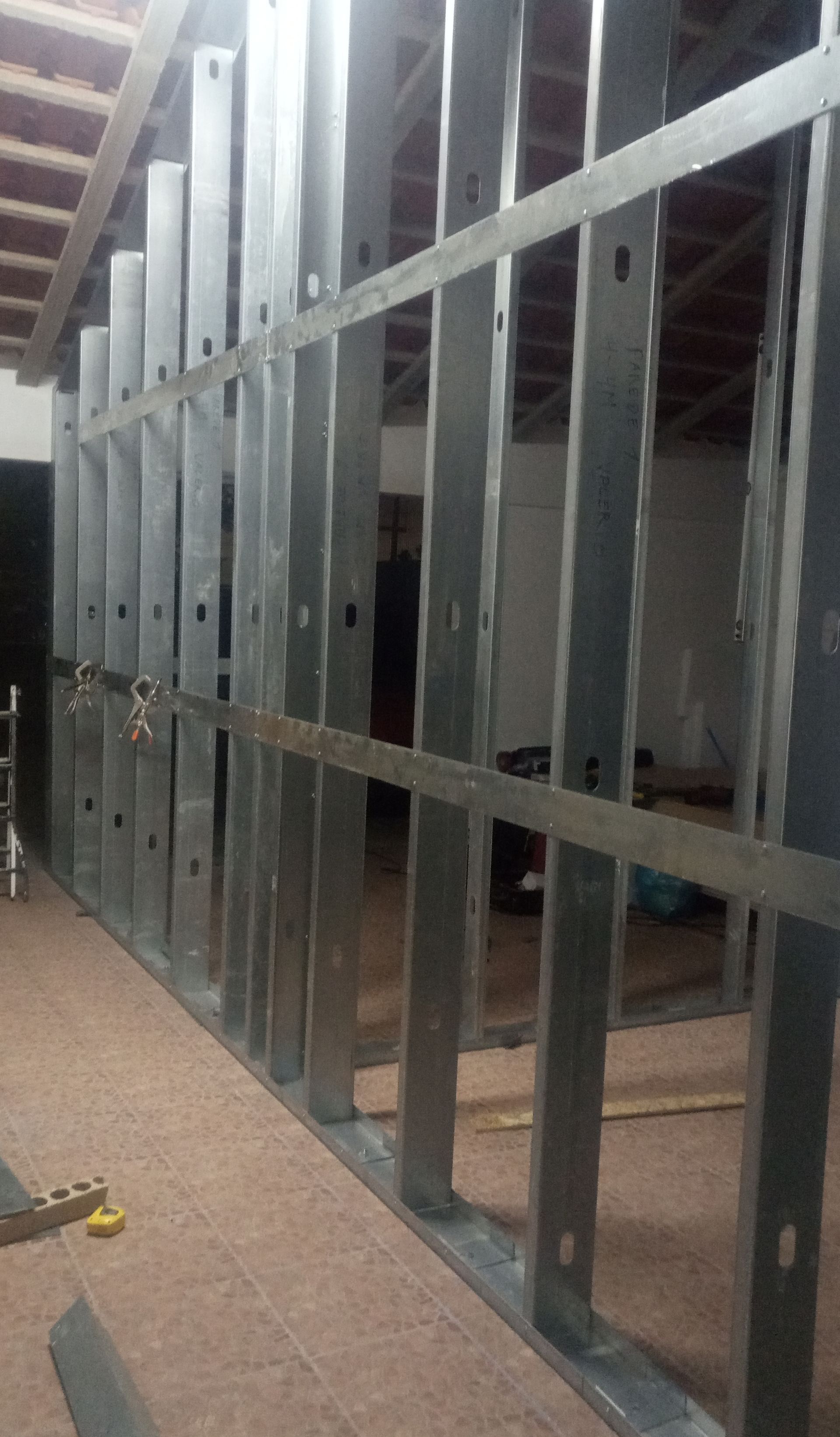 Estrutura metálica emoldurando uma parede, em ambiente interno, com suportes horizontais. Construção em andamento.