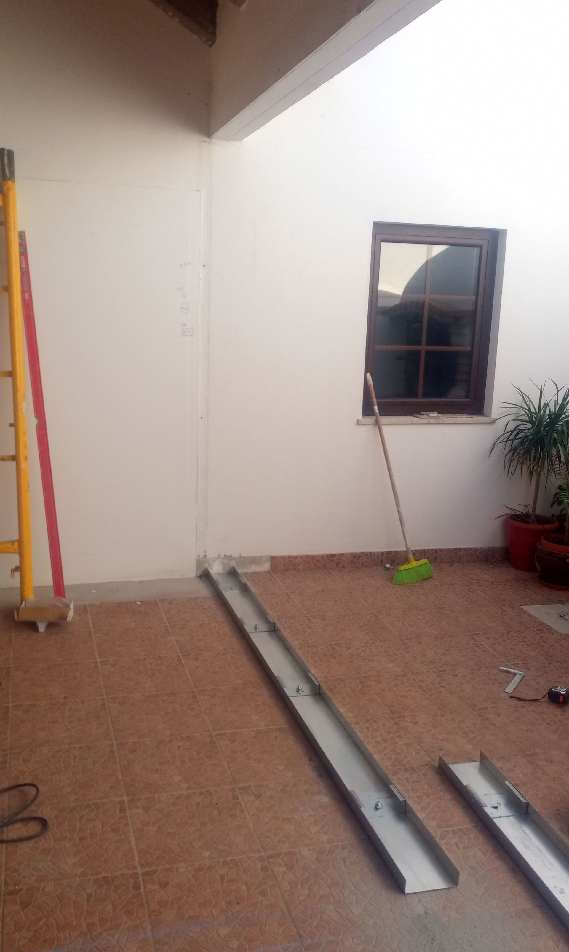 Foto de ambiente interno com rampas de metal sobre piso de azulejo, perto de uma janela, escada e vassoura.