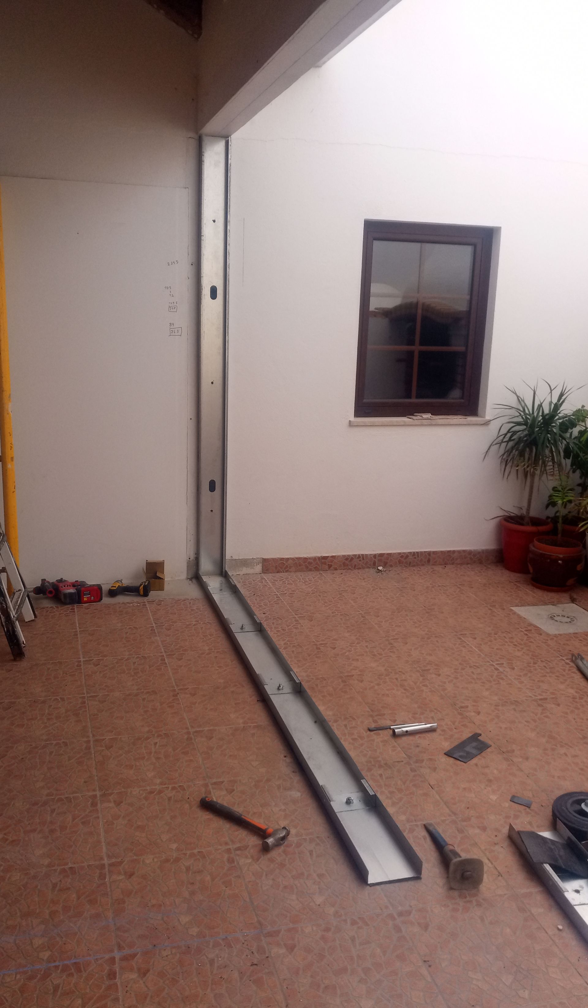 Construção: estrutura metálica instalada em um pátio, pronta para receber a parede. Ferramentas espalhadas por perto.