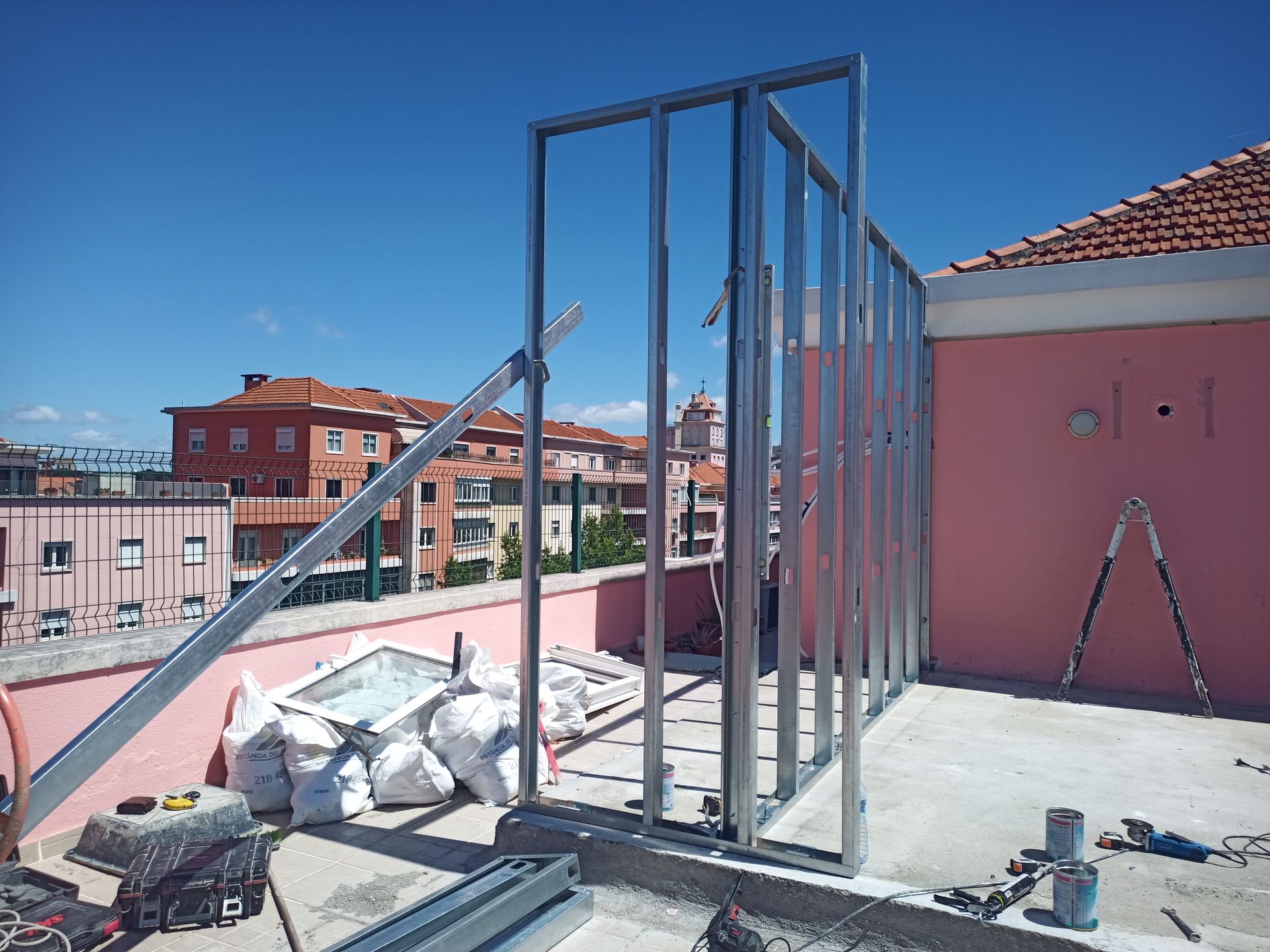 Estrutura metálica para uma parede externa em um telhado, com materiais de construção e paisagem urbana visíveis.