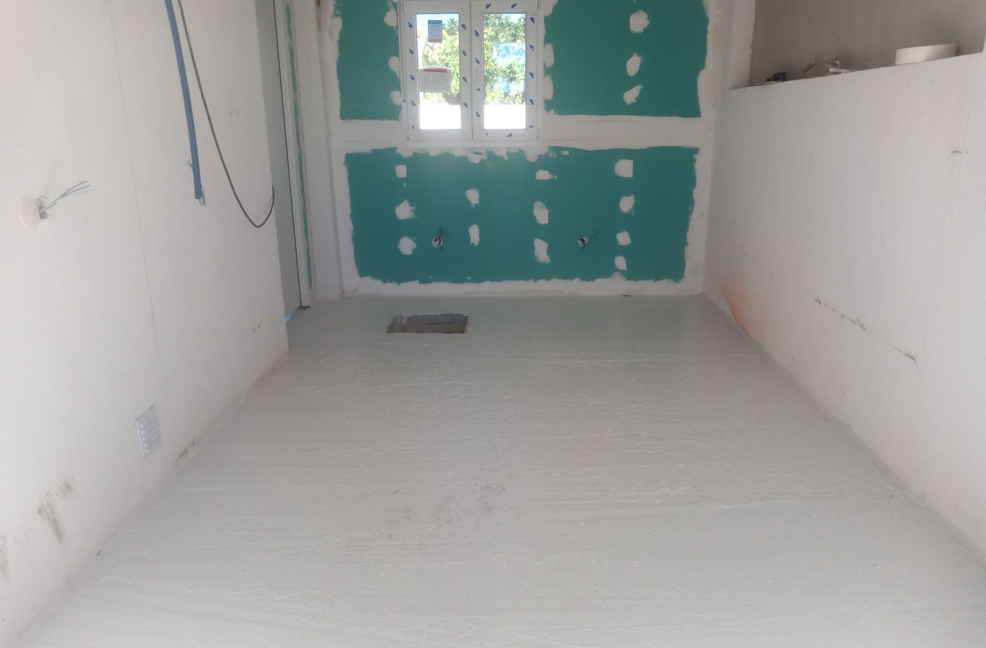 Quarto interno em construção com drywall verde e paredes e piso brancos. Janela nos fundos.