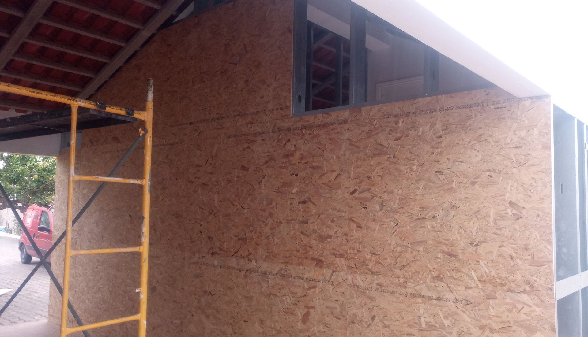 Parede externa em construção com painéis de madeira marrom, andaimes e uma moldura de janela.