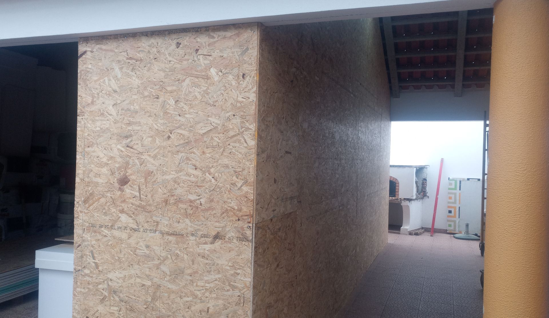 Vista interior: parede de madeira rústica na entrada, que dá acesso a uma área externa com equipamentos visíveis.