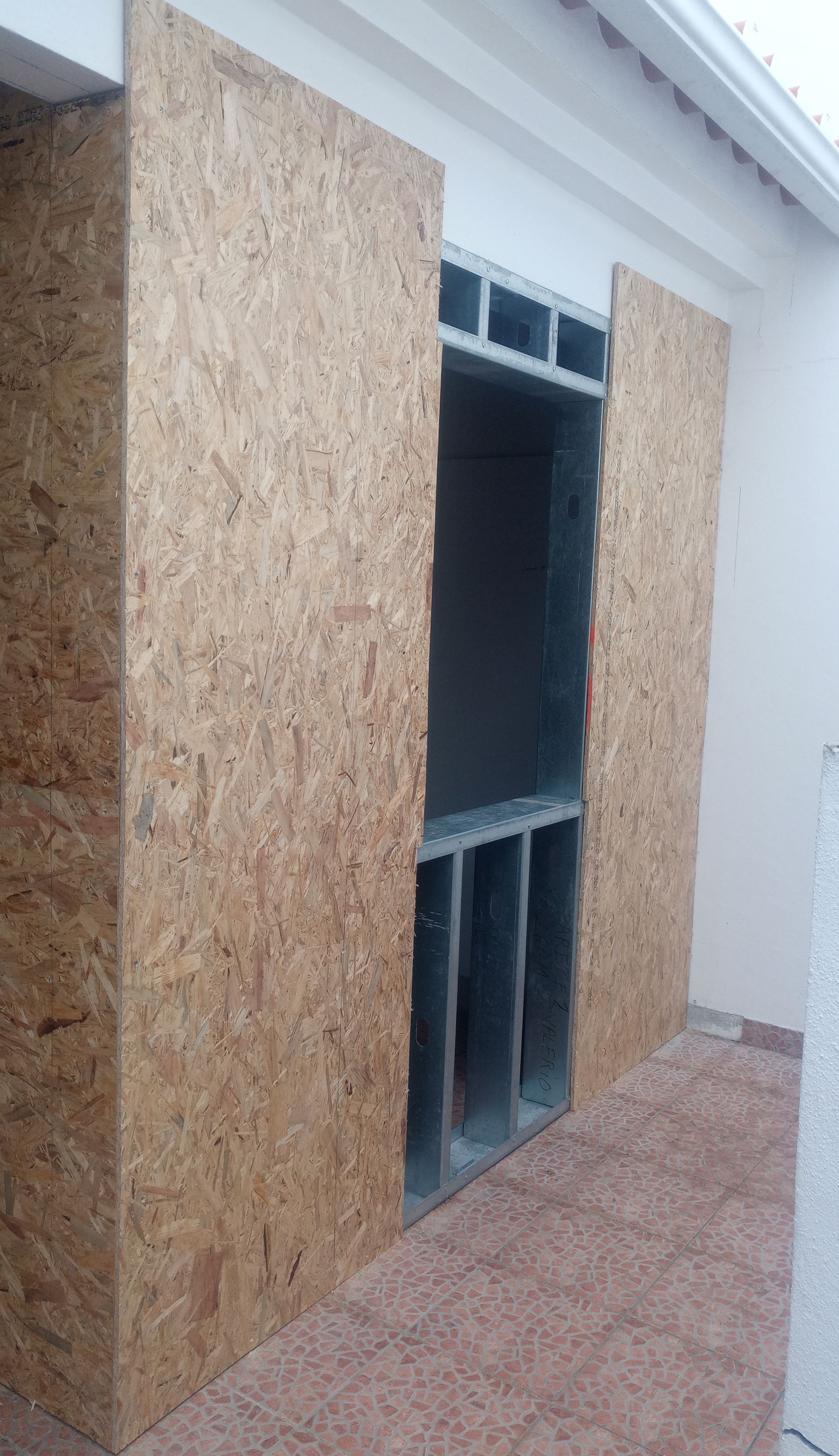 Placas de OSB cobrem parcialmente uma parede externa inacabada com uma abertura de estrutura metálica.