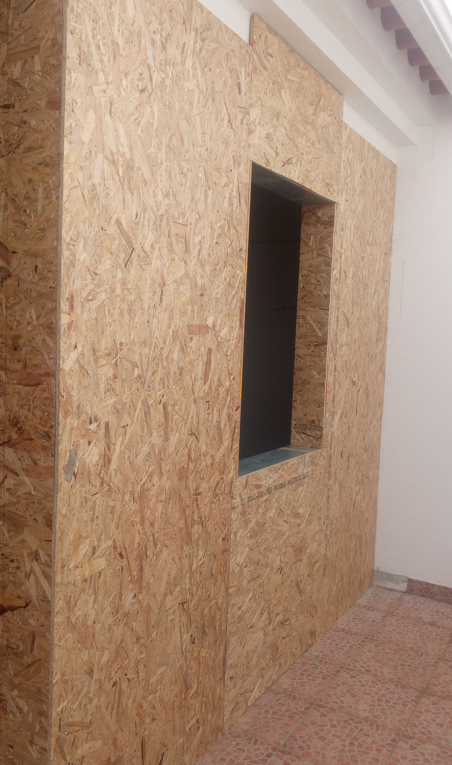 Parede revestida com painéis OSB e com abertura para janela; marrom claro com interior escuro; ambiente interno.