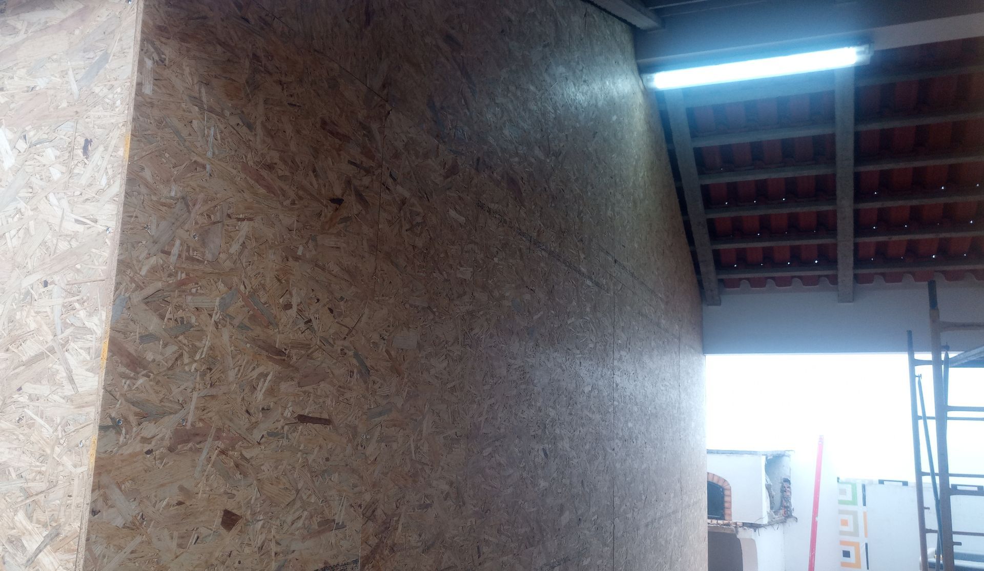 Parede de placa OSB com telhado parcialmente visível e uma luminária no teto.
