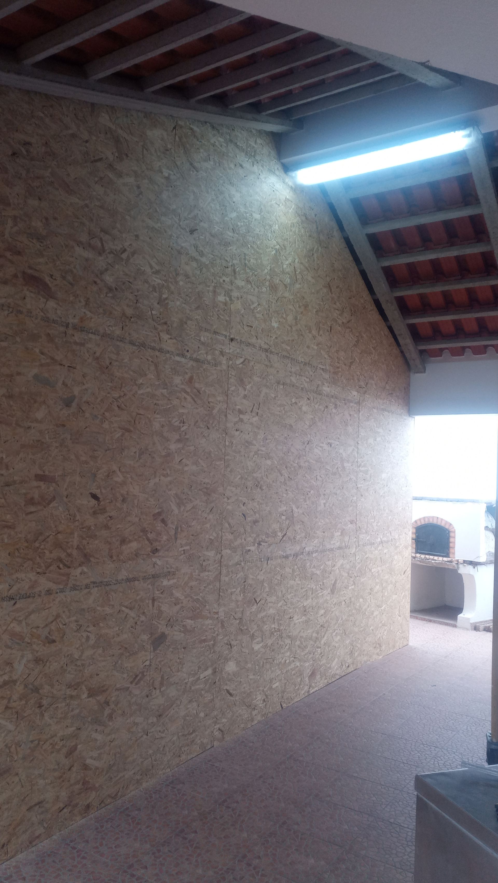 Parede de OSB sob um telhado inclinado com uma porta aberta para um pátio.