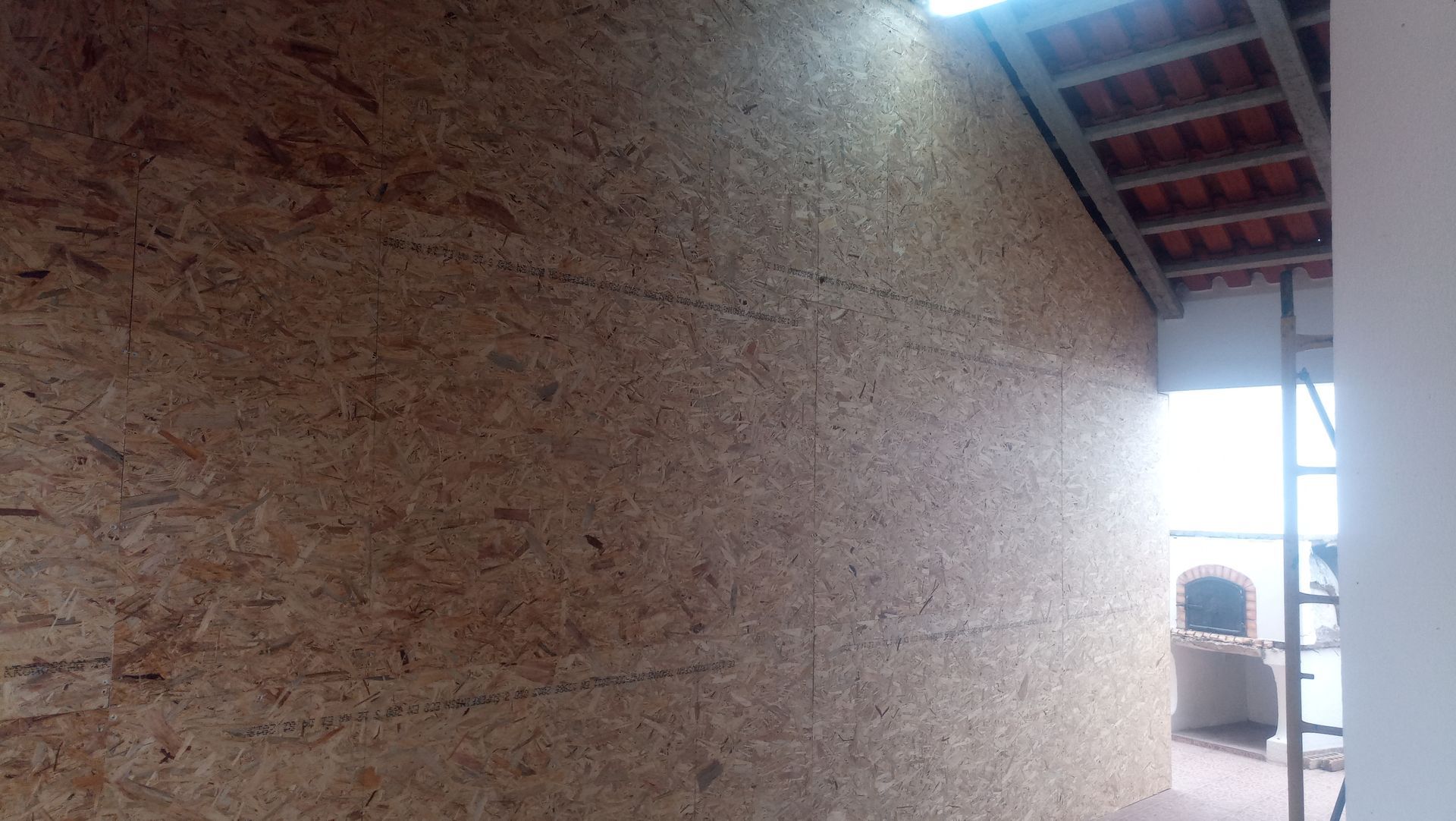 Construção de parede revestida com OSB, marrom claro com telhas visíveis.