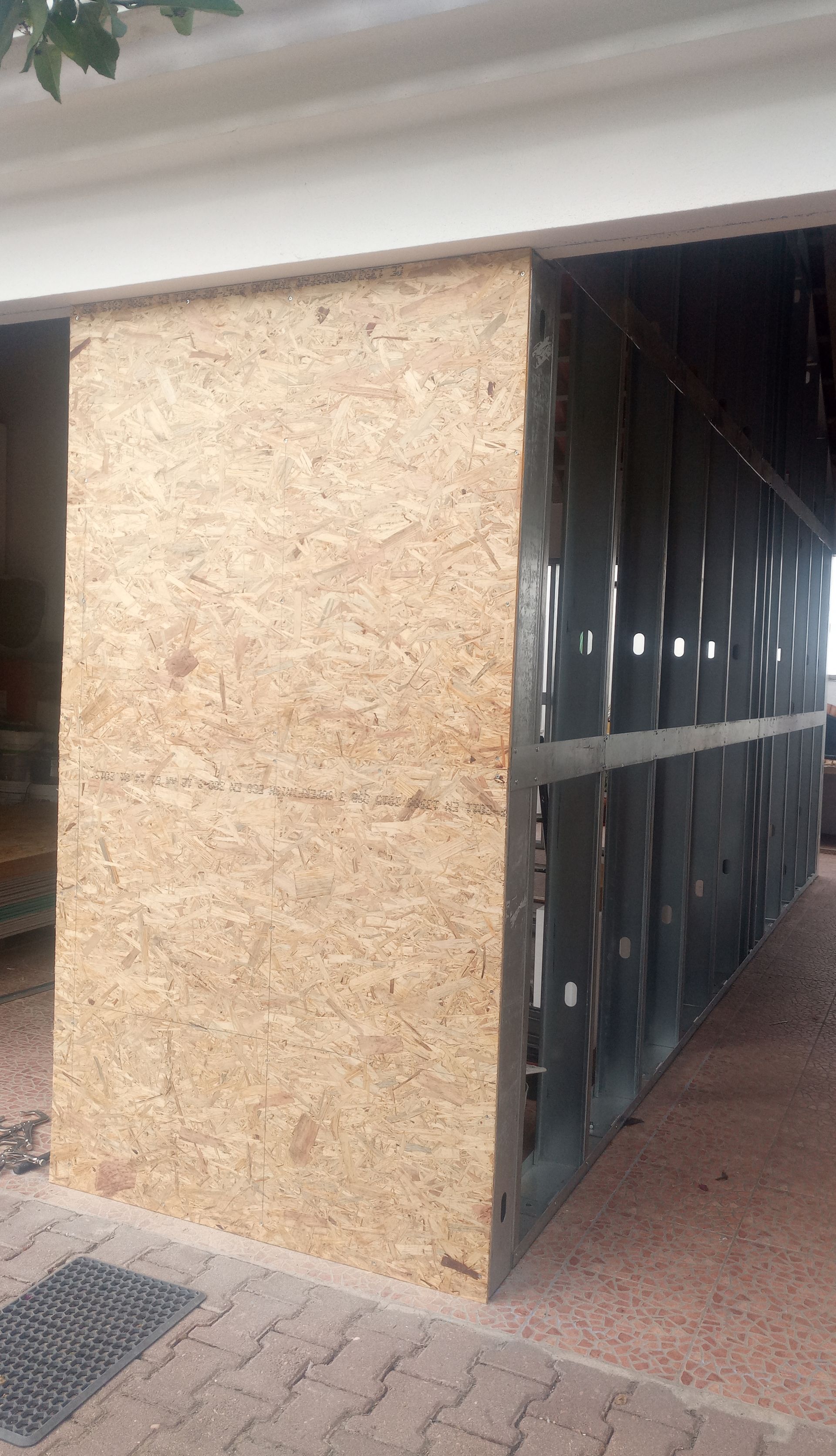 Construção de parede parcial com revestimento em aglomerado e estrutura metálica. Localizada em garagem ou área de estacionamento coberta.