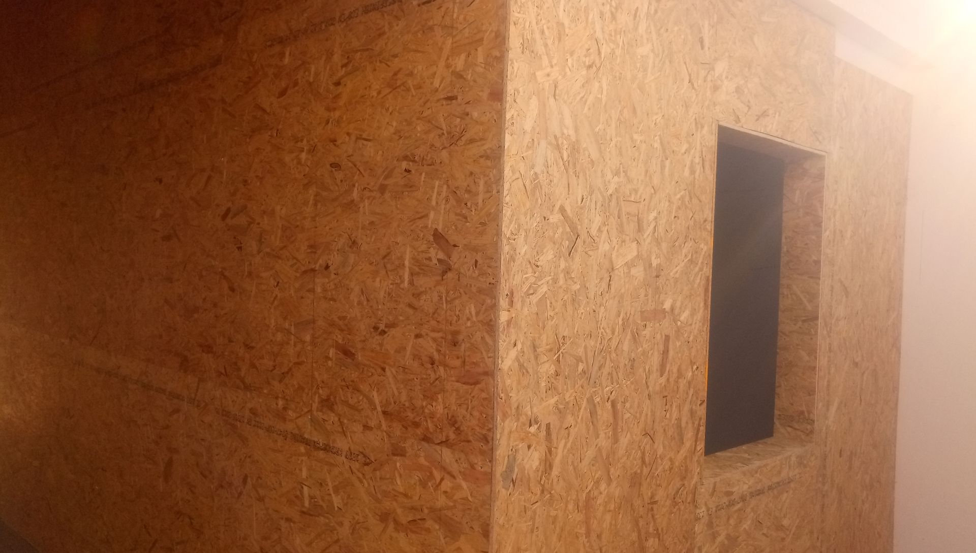 Canto de uma estrutura de madeira com uma abertura retangular, possivelmente uma janela ou porta. Tons de marrom.