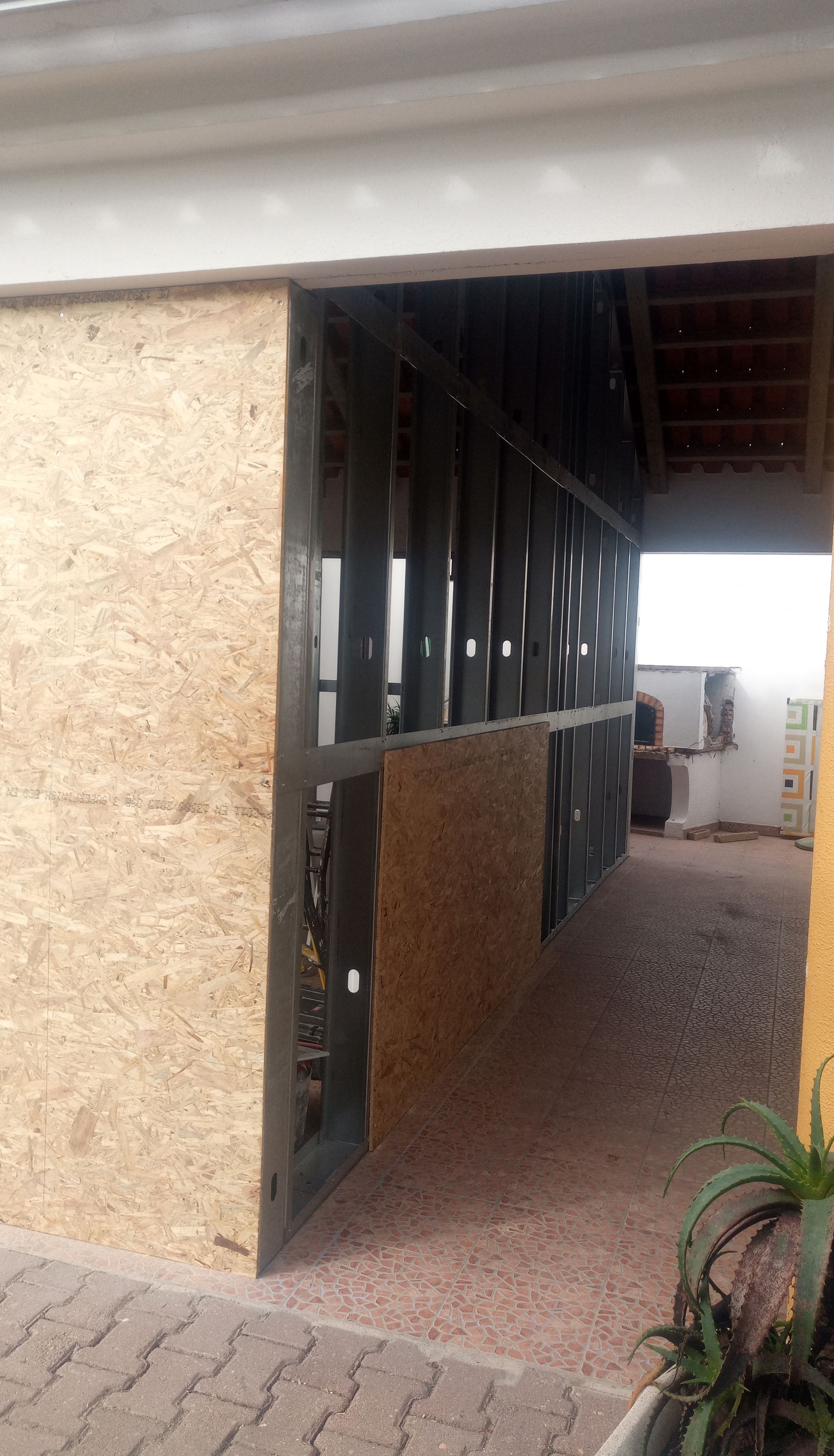 Entrada de um edifício com estrutura metálica escura e parede texturizada em tom bege.