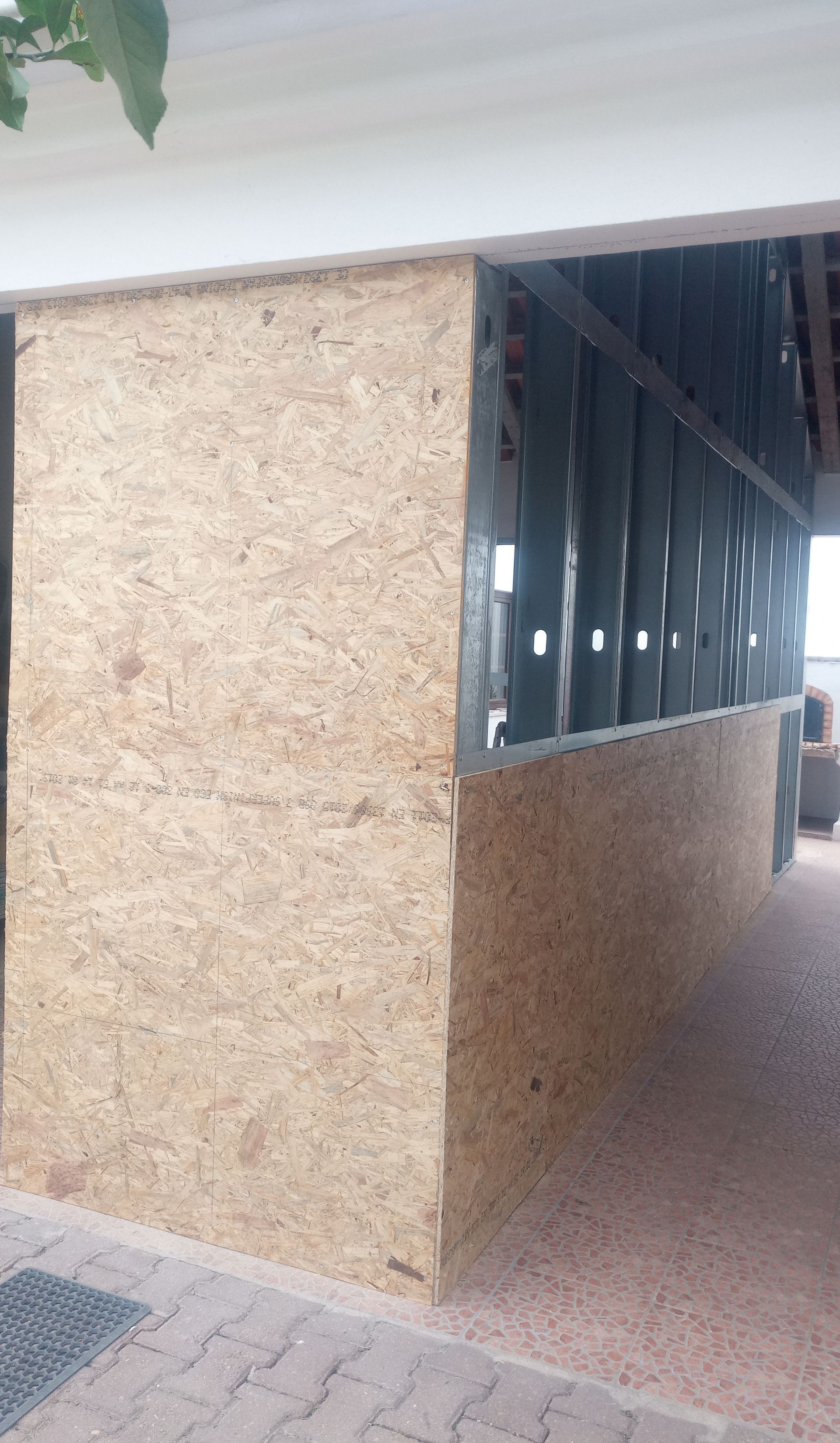 Parede externa feita de placas de madeira composta com estrutura metálica. Piso pavimentado.